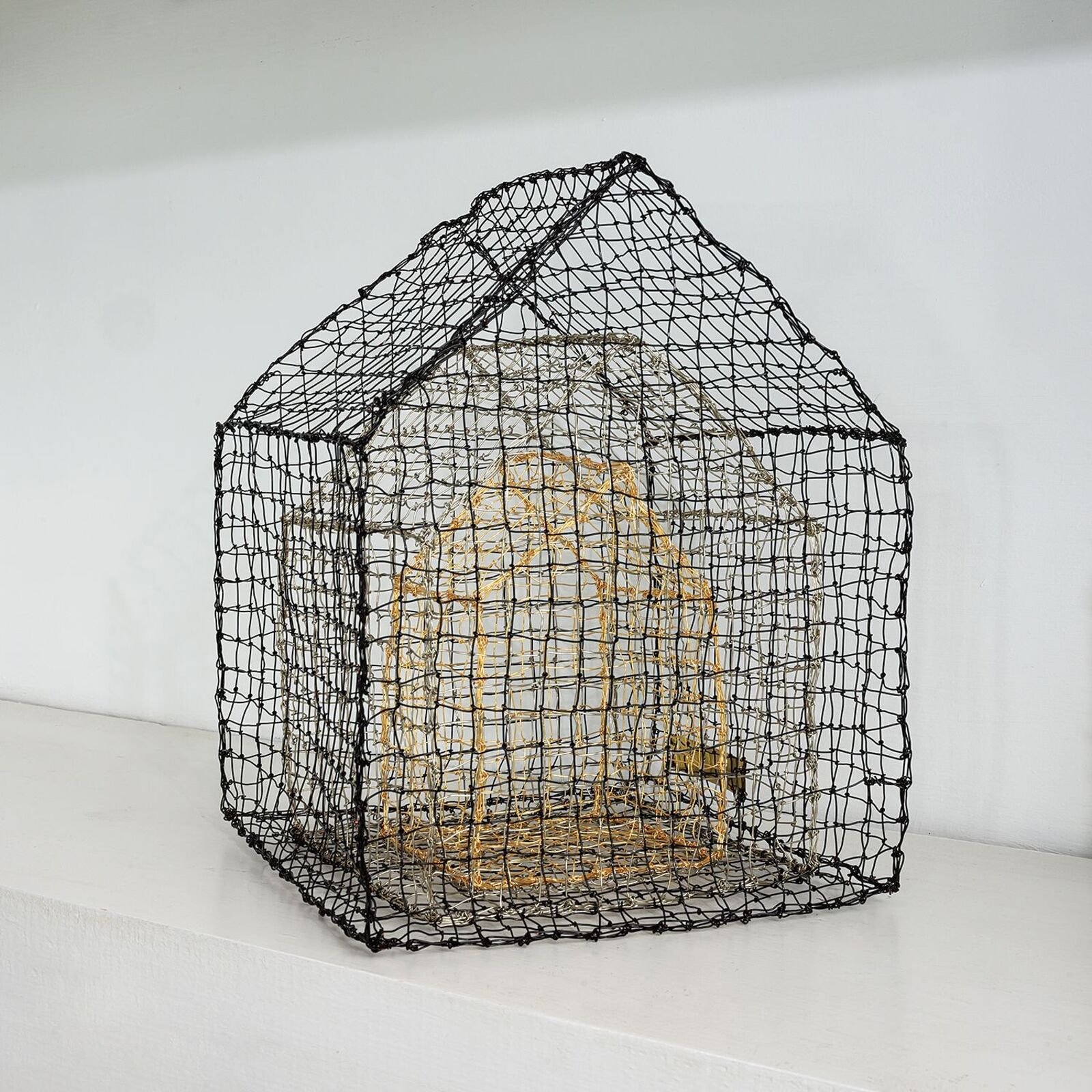A wireframe house sculpture with a golden interior structure.