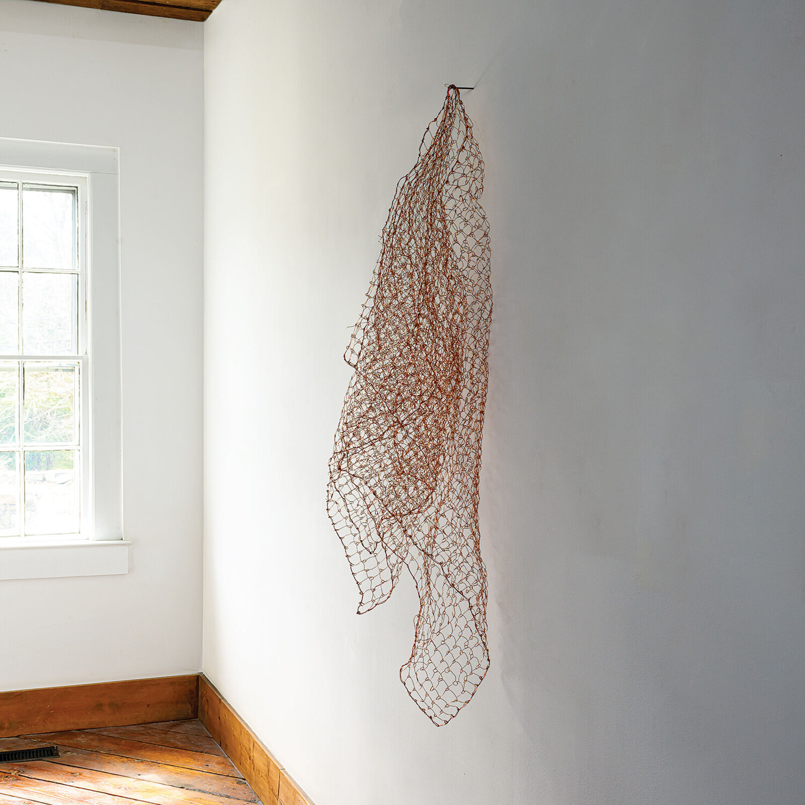 A minimalist interior scene featuring a suspended copper wire mesh sculpture against a plain wall.