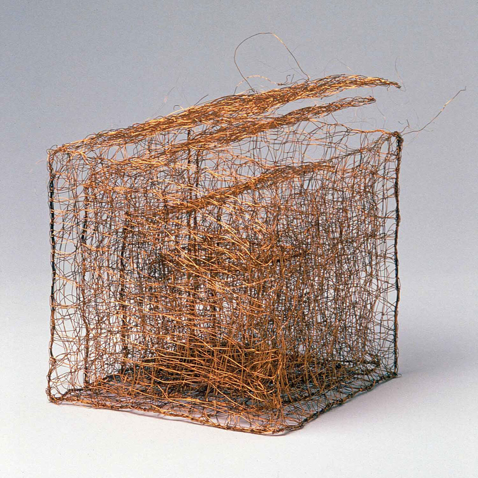 A copper wire sculpture shaped like a basket with three upward flaring tendrils.