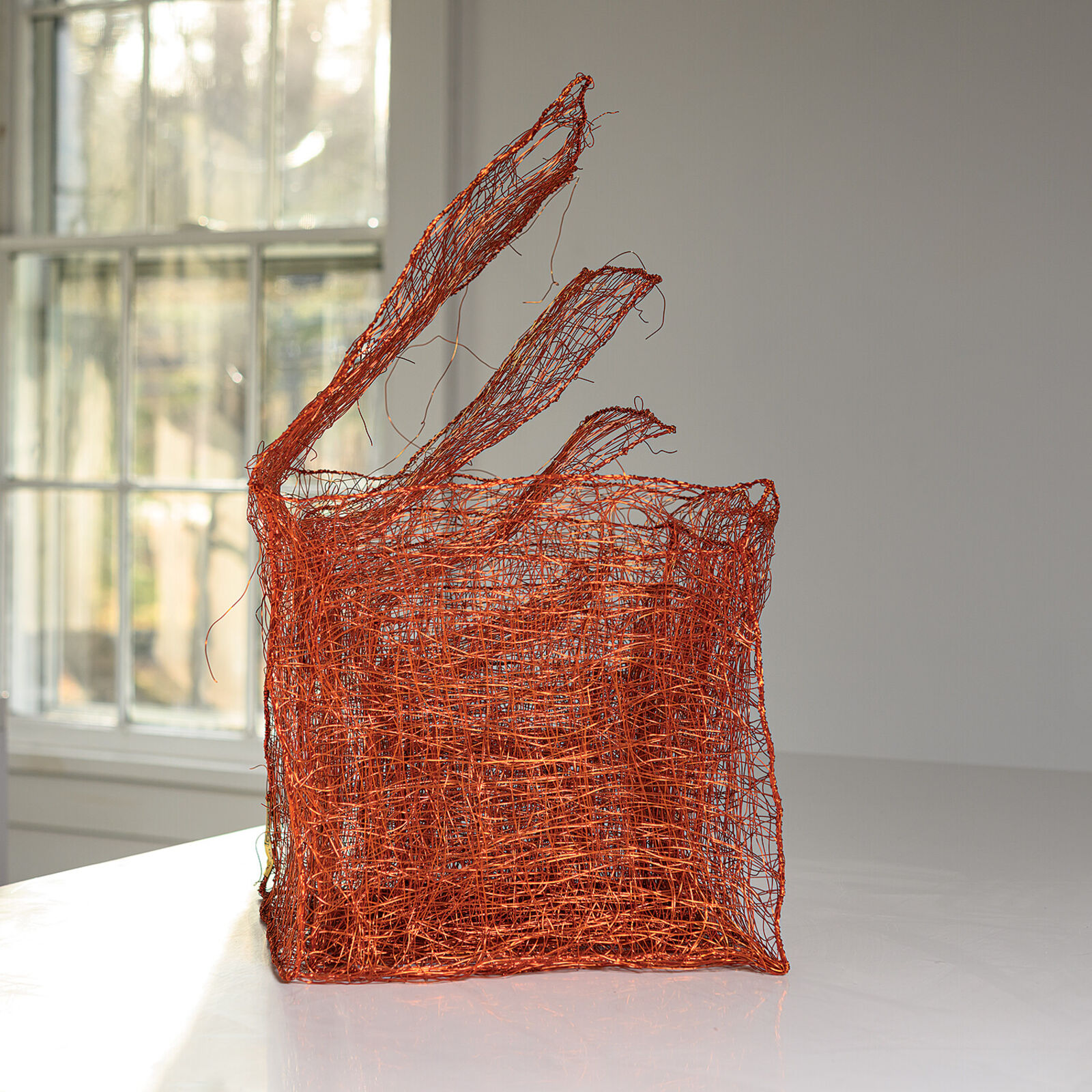 A copper wire sculpture shaped like a basket with three upward flaring tendrils.