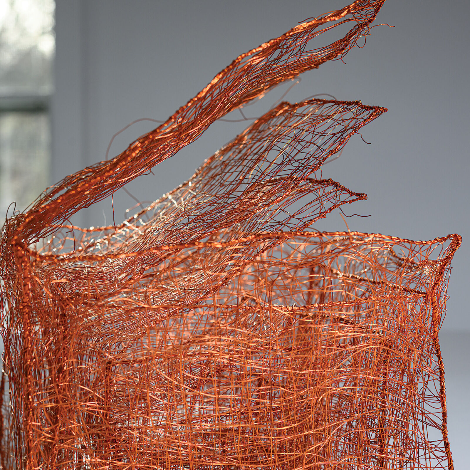 A copper wire sculpture shaped like a basket with three upward flaring tendrils.