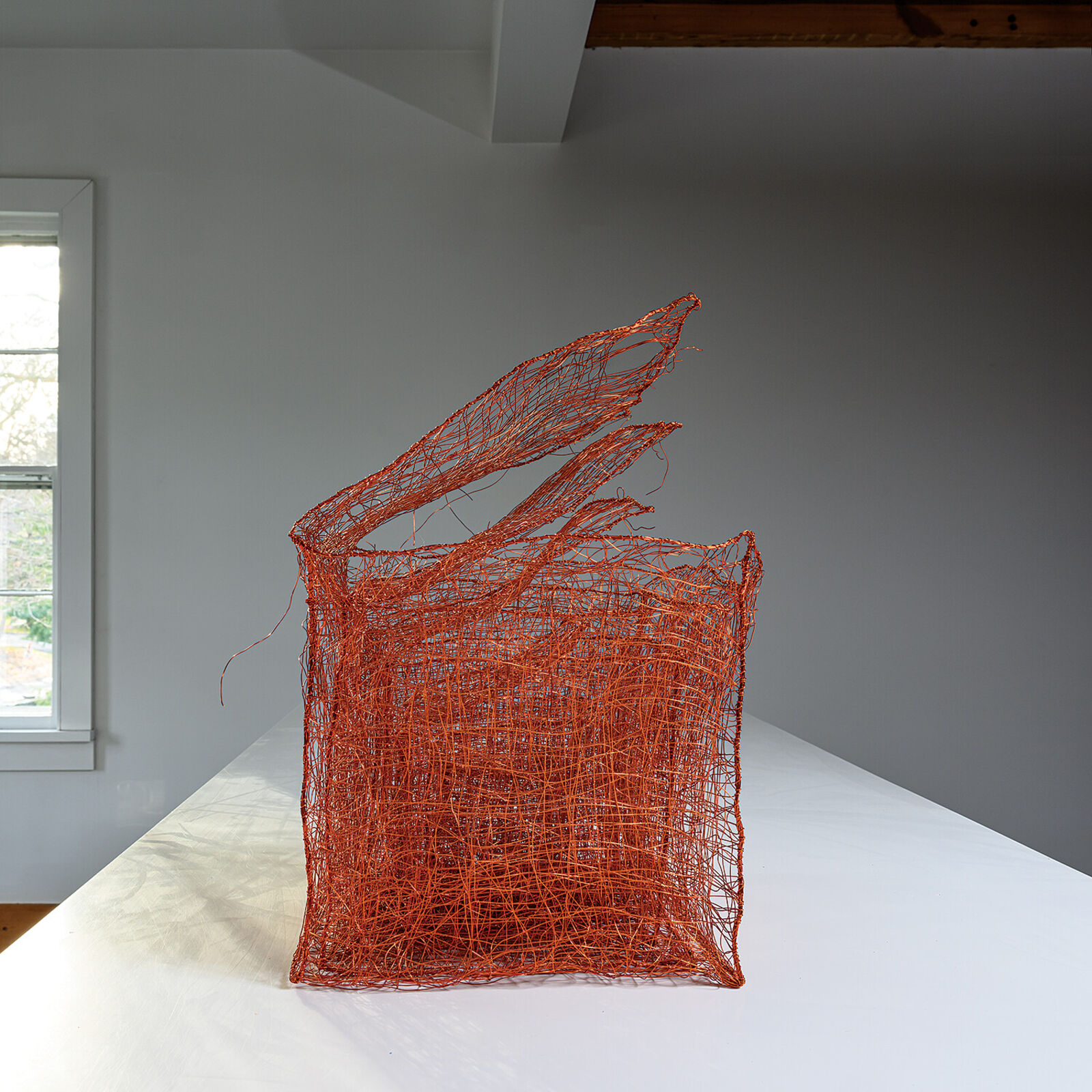 A copper wire sculpture shaped like a basket with three upward flaring tendrils.