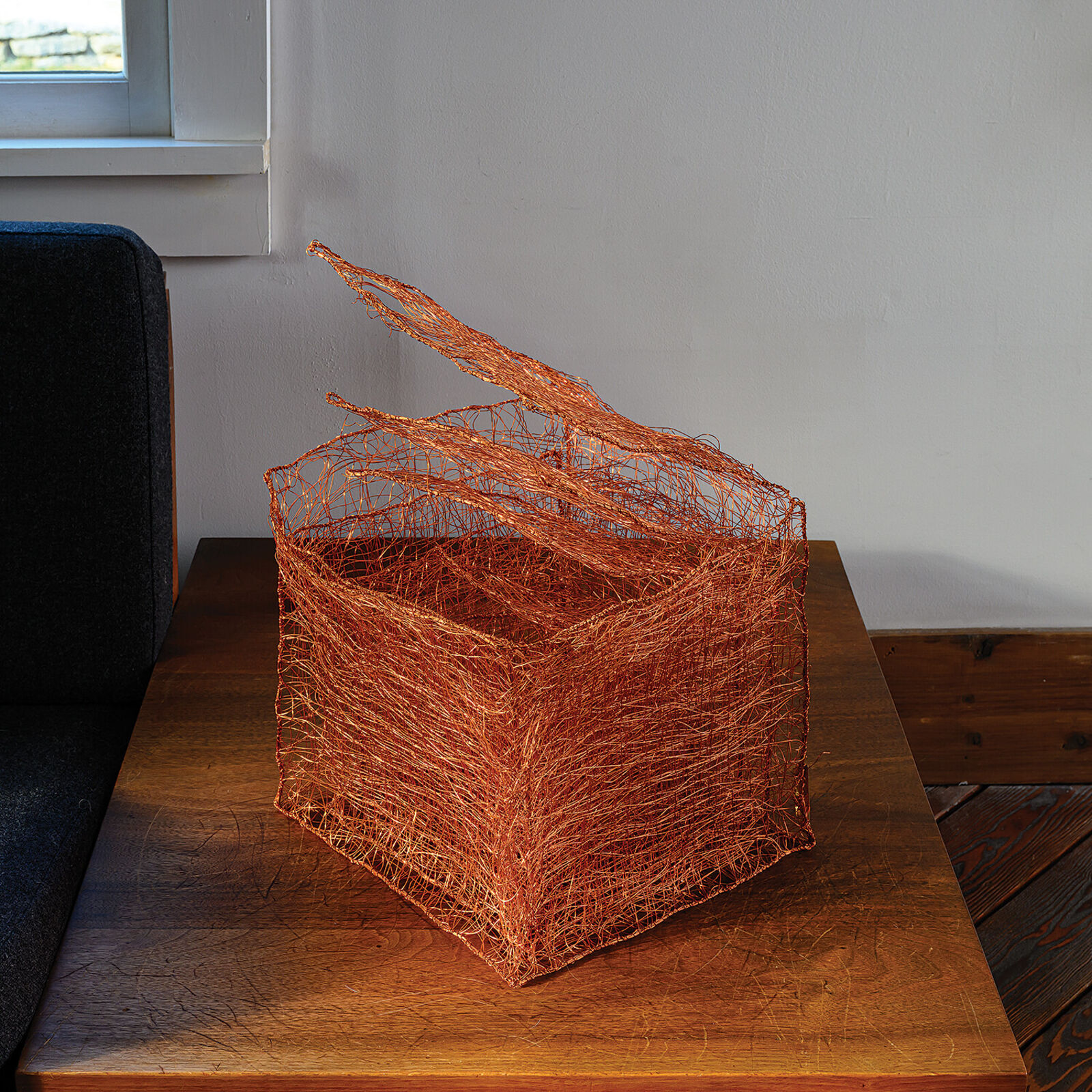 A copper wire sculpture shaped like a basket with three upward flaring tendrils.