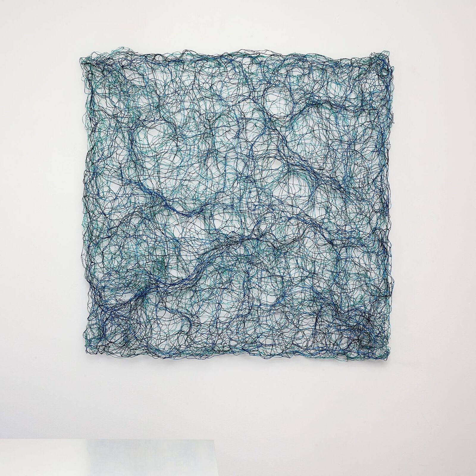 A square wire sculpture with a tangled, organic pattern in shades of blue and black against a white background.