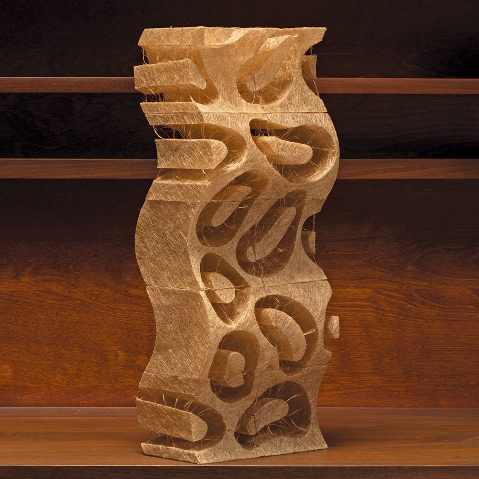 A light-colored, vertically oriented sculpture with a wavy form and intricate cut-out patterns.