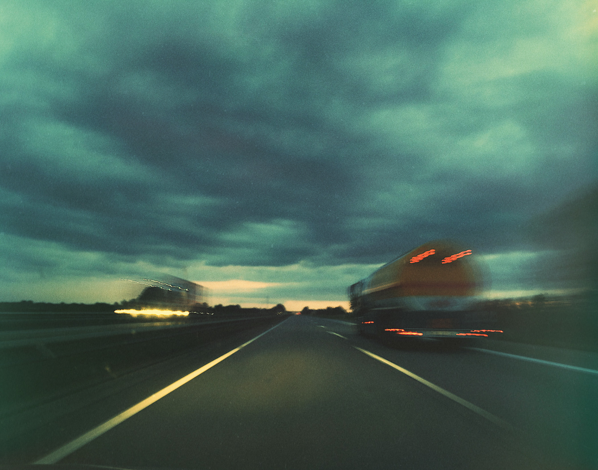A car driving down a highway under a cloudy sky.