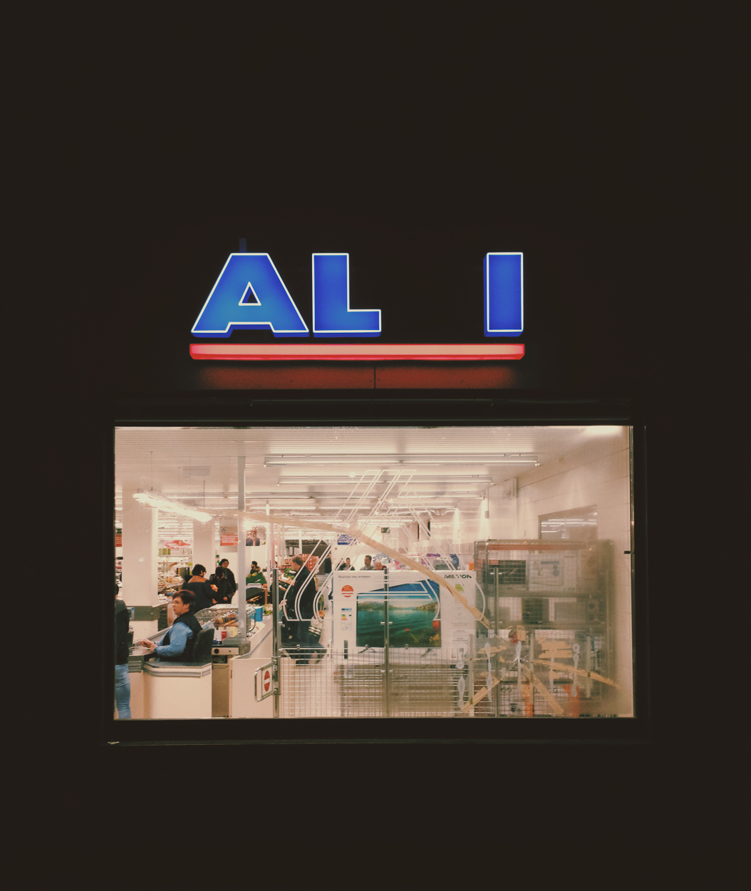 A vertical composition of a storefront with a blue neon sign and a window view into a brightly lit interior.