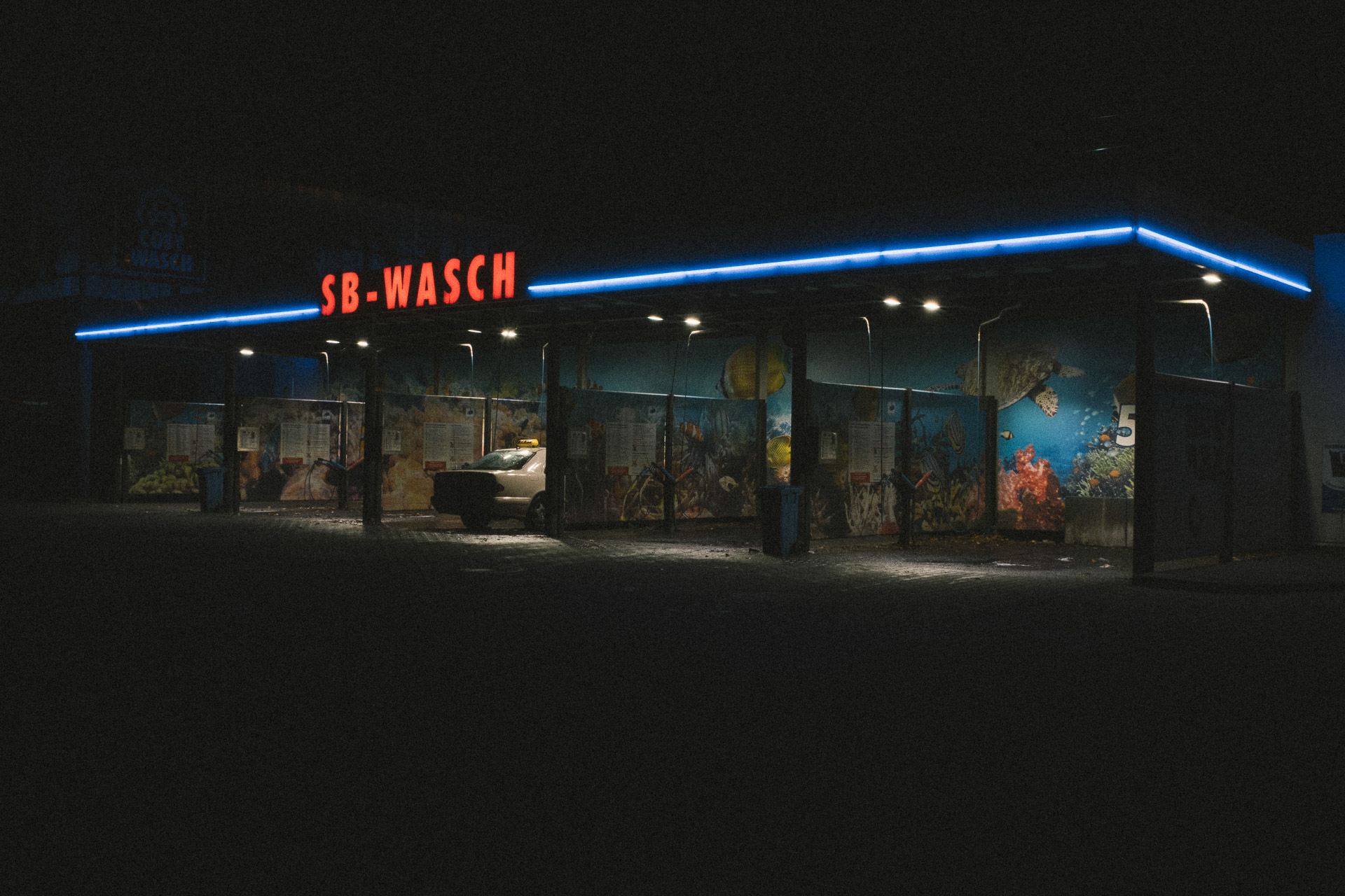 A car is parked in front of a gas station at night.