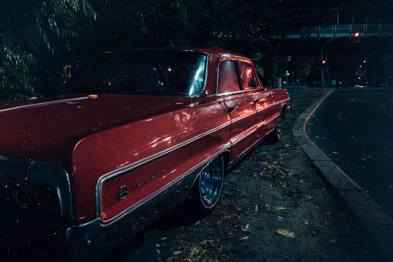 A red car parked on the side of a road at night.