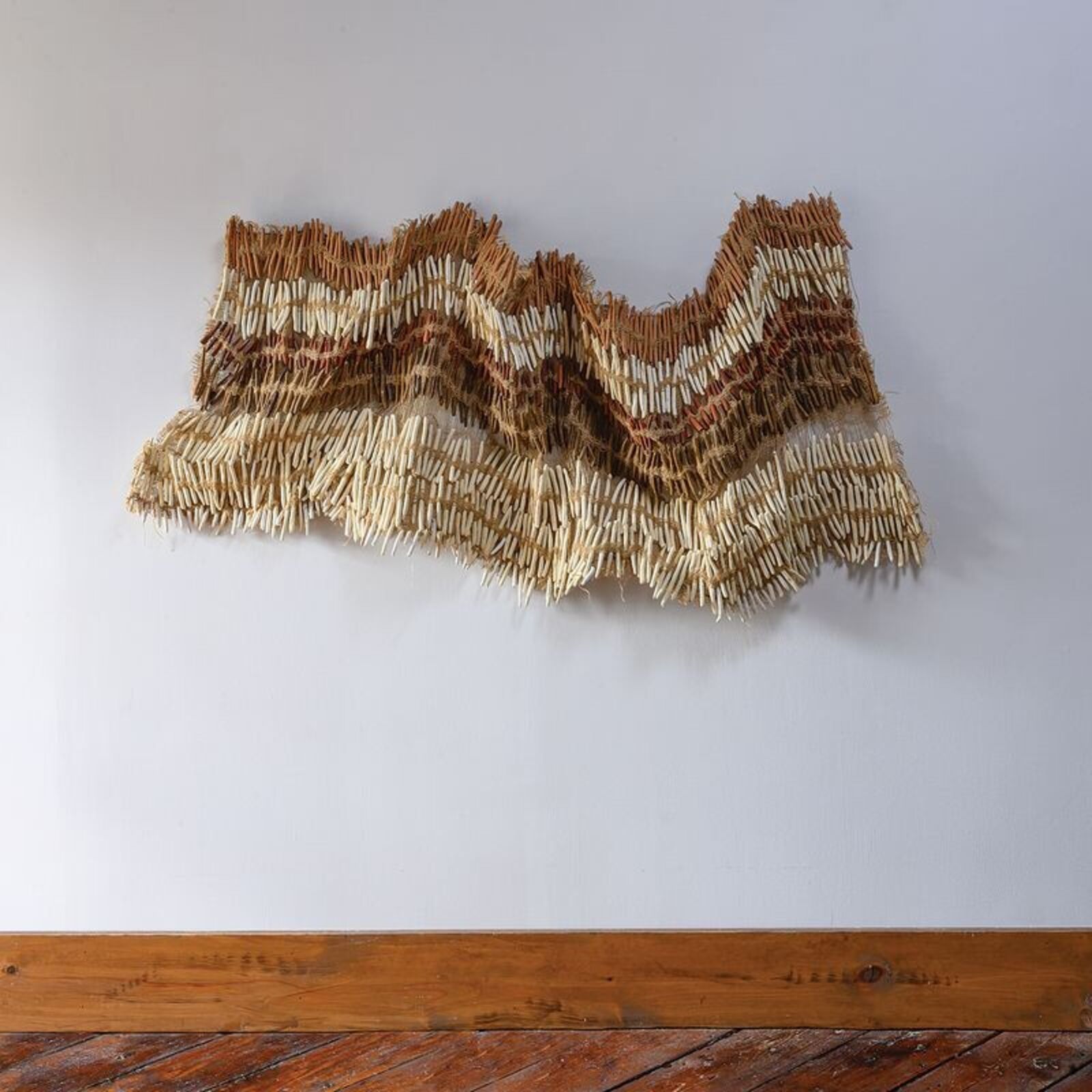 A textured wall art piece made of natural fibers with a wavy, layered design.