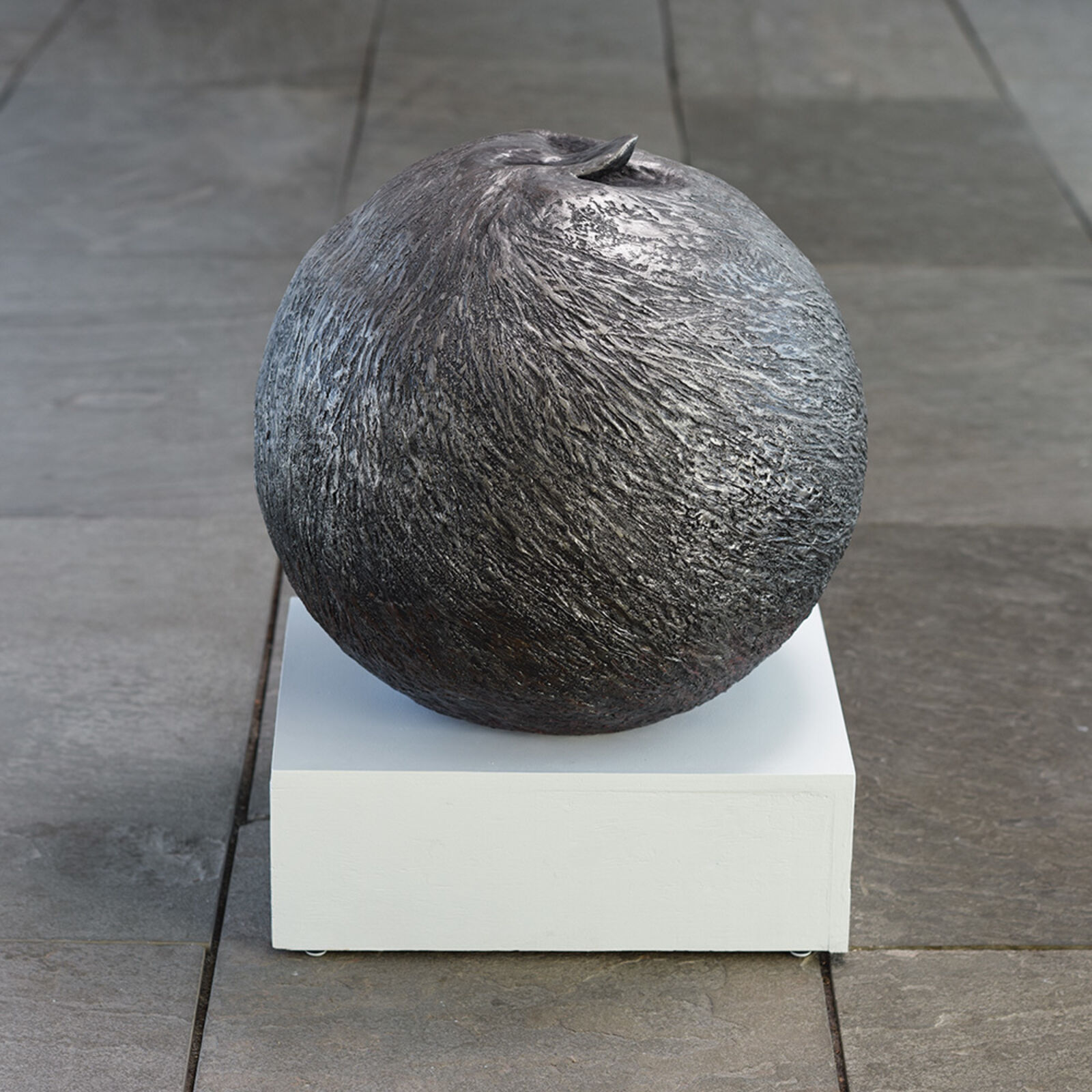A textured, dark sphere sculpture resting on a white pedestal.