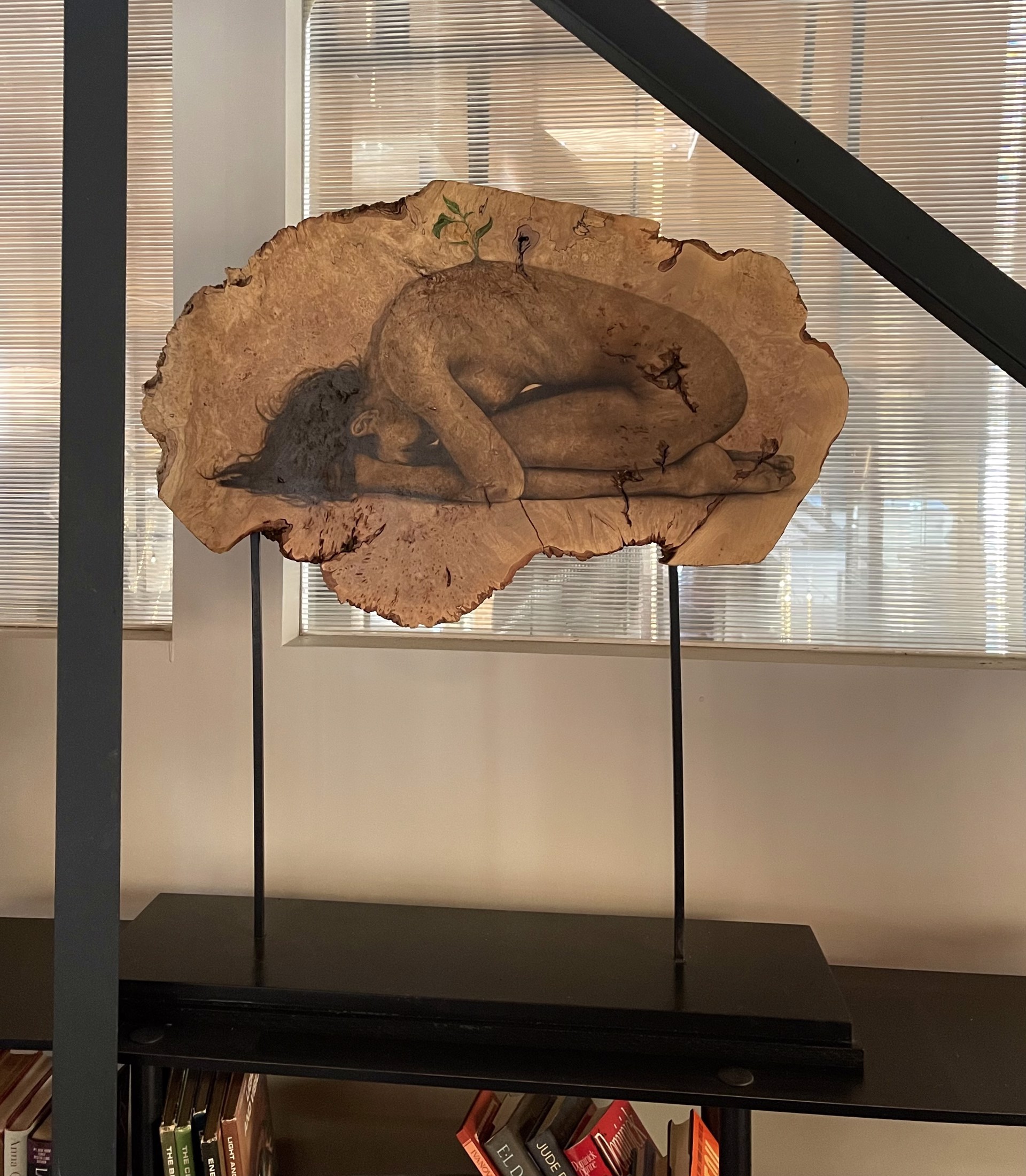 A sculpture of a woman laying down on a piece of wood.