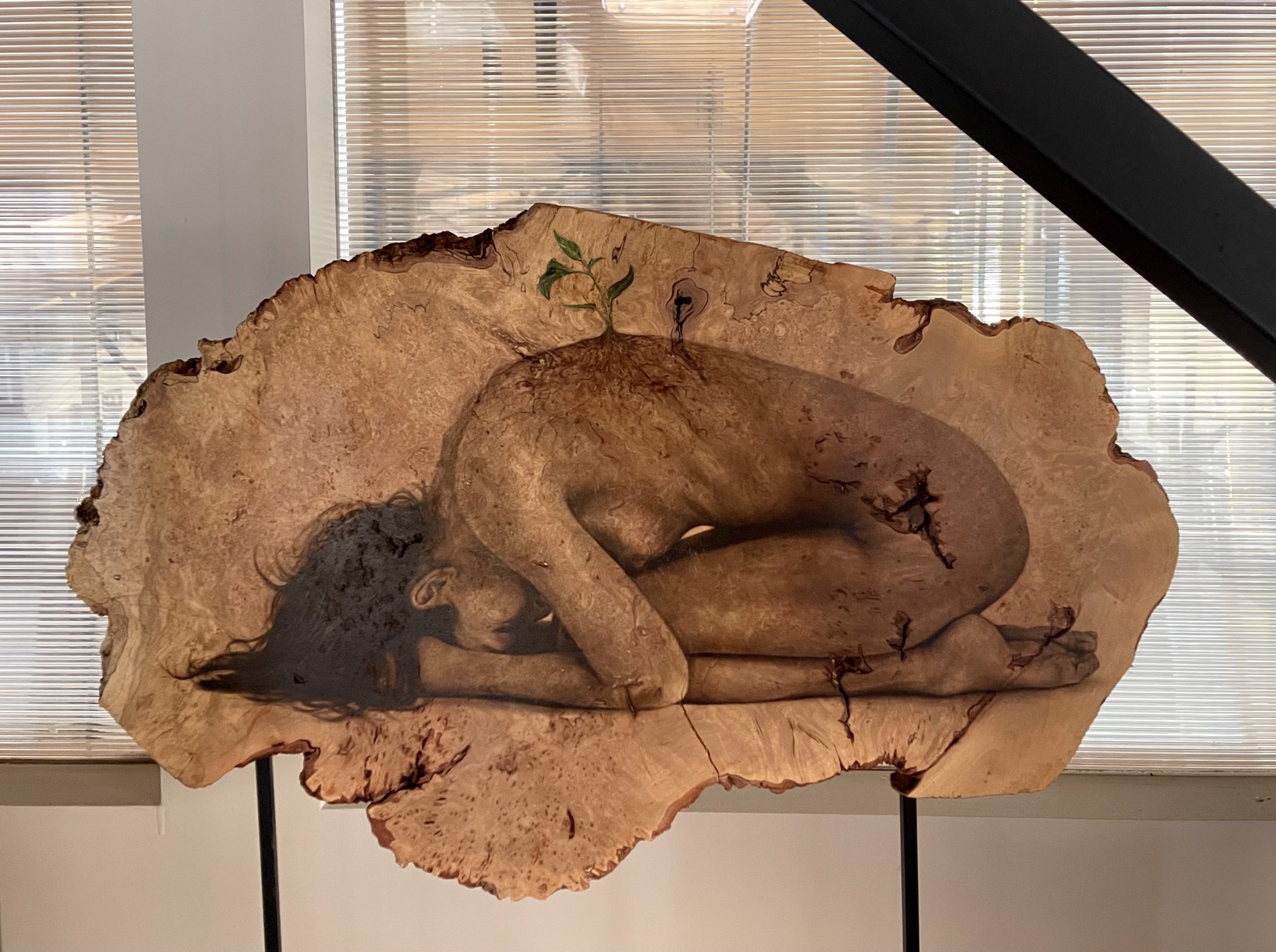 A sculpture of a woman laying down on a piece of wood.