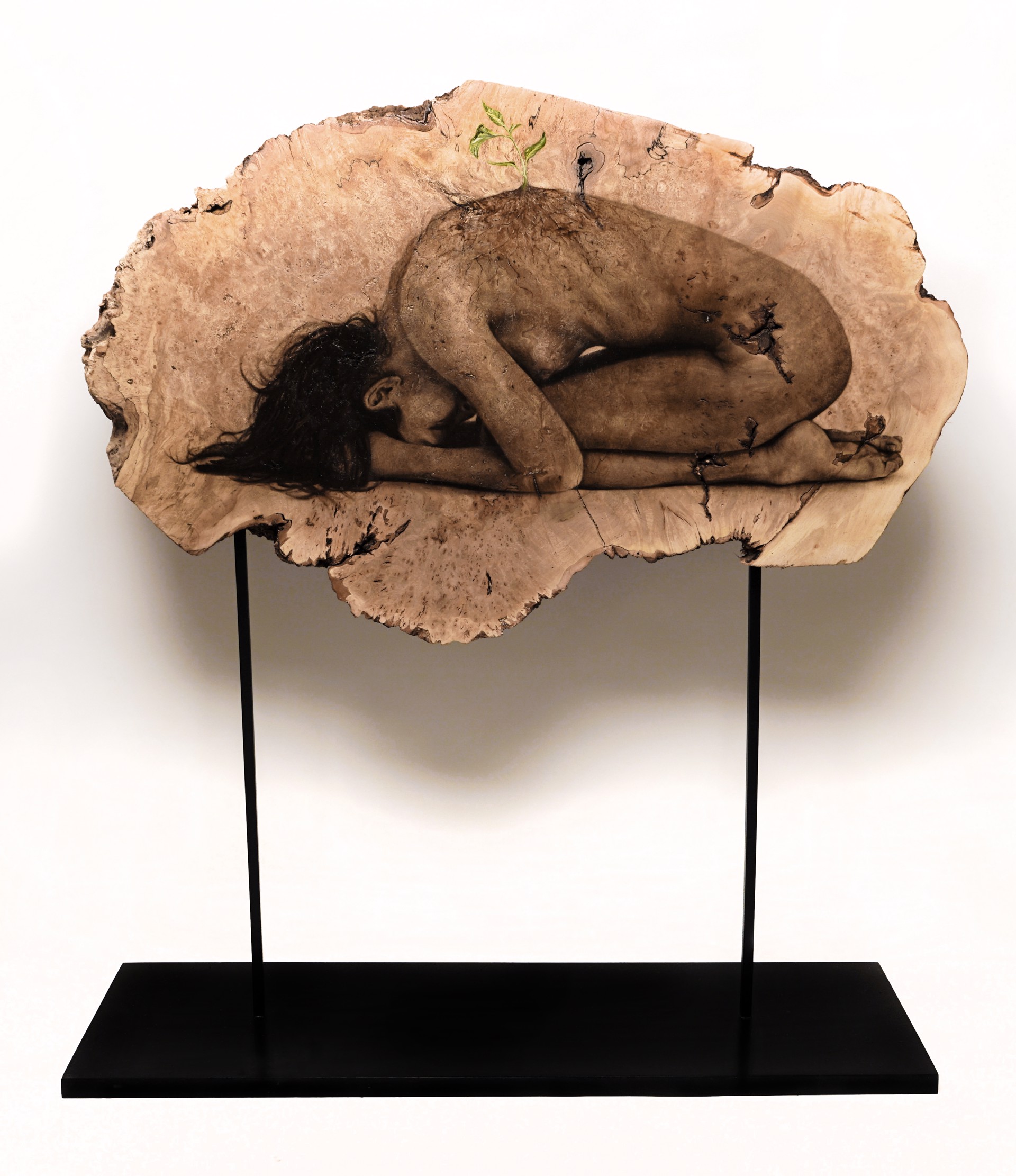 A sculpture of a woman laying down on a piece of wood.