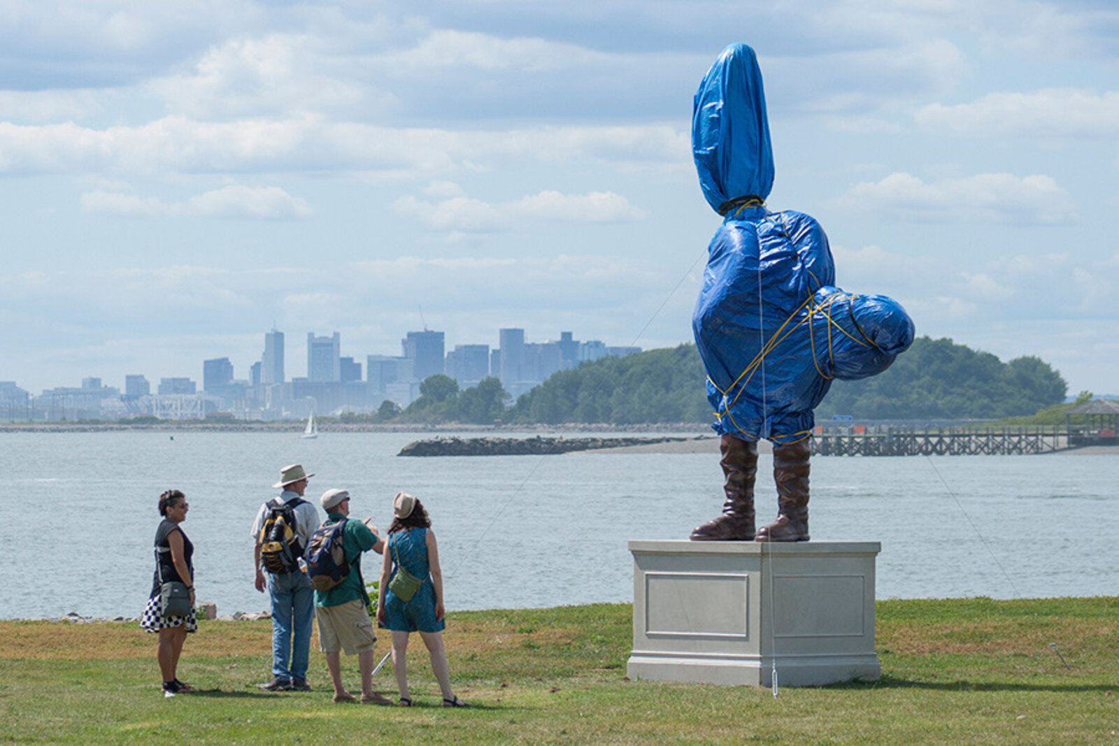 A surreal outdoor sculpture of a figure in blue plastic and boots standing on a pedestal.