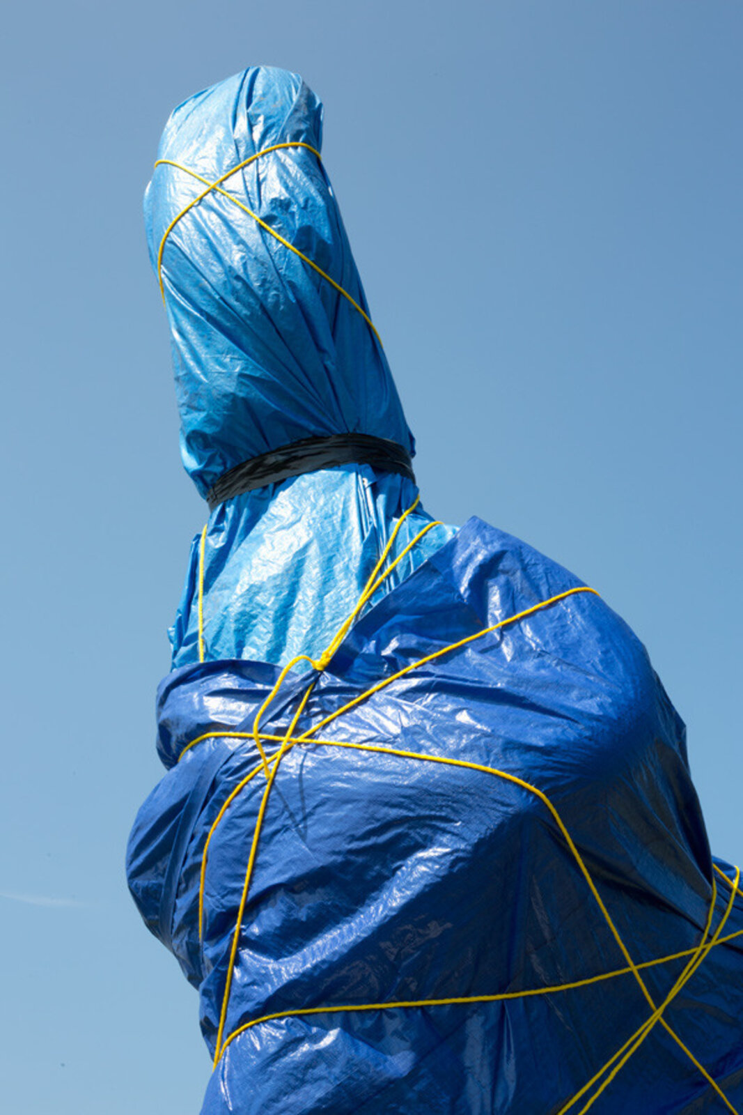 A surreal outdoor sculpture of a figure in blue plastic and boots standing on a pedestal.