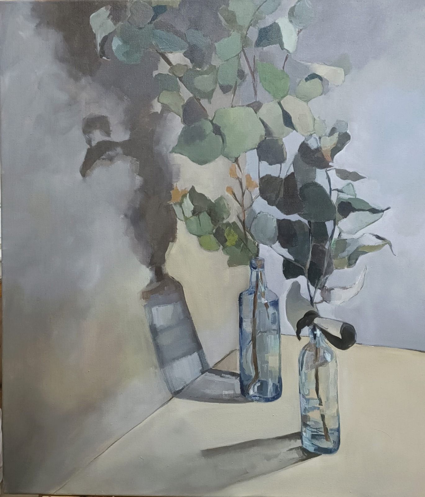 A quiet still life featuring three glass bottles holding green foliage against a soft, shadowed background.