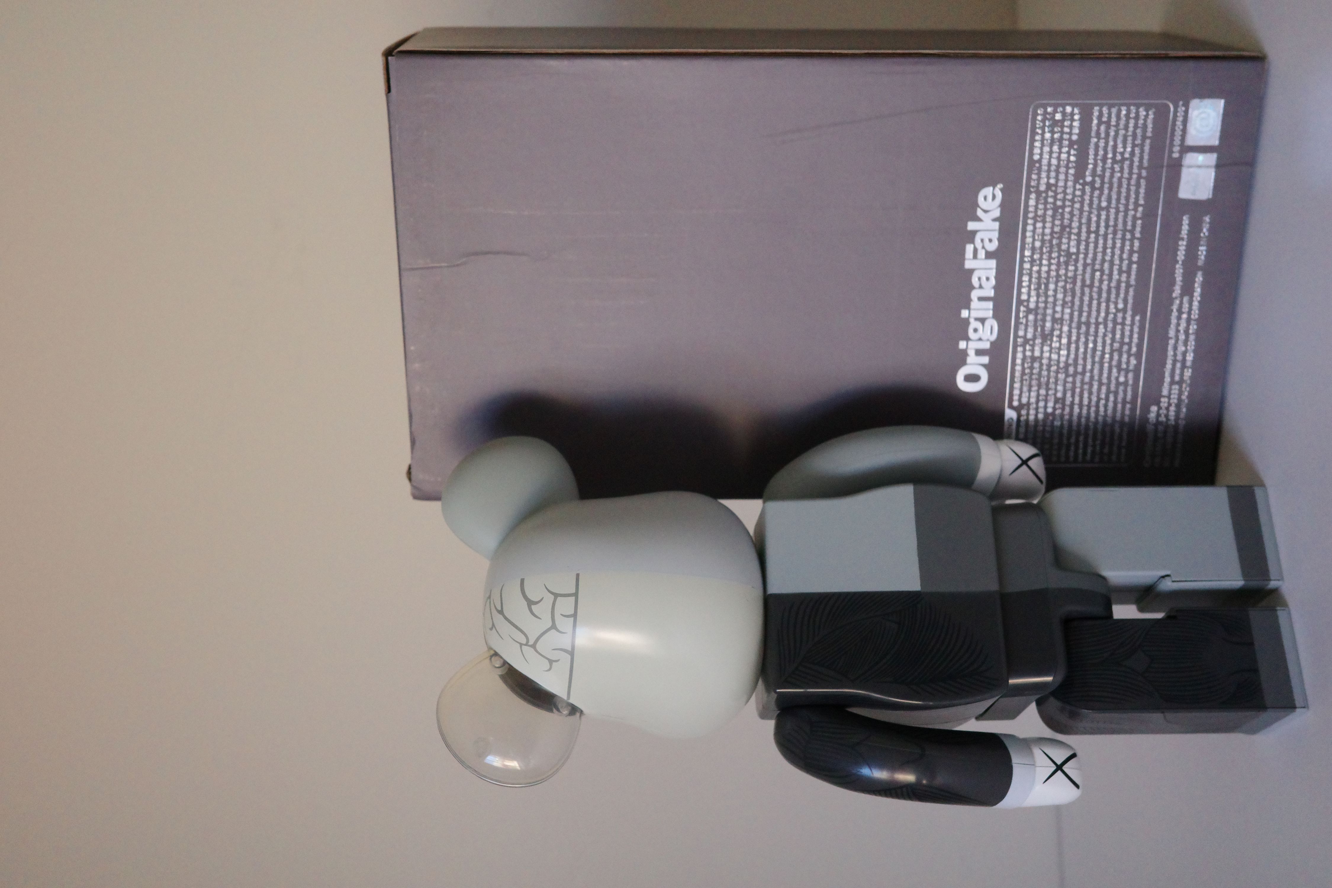 A gray and black bearbrick with a box on a white surface.