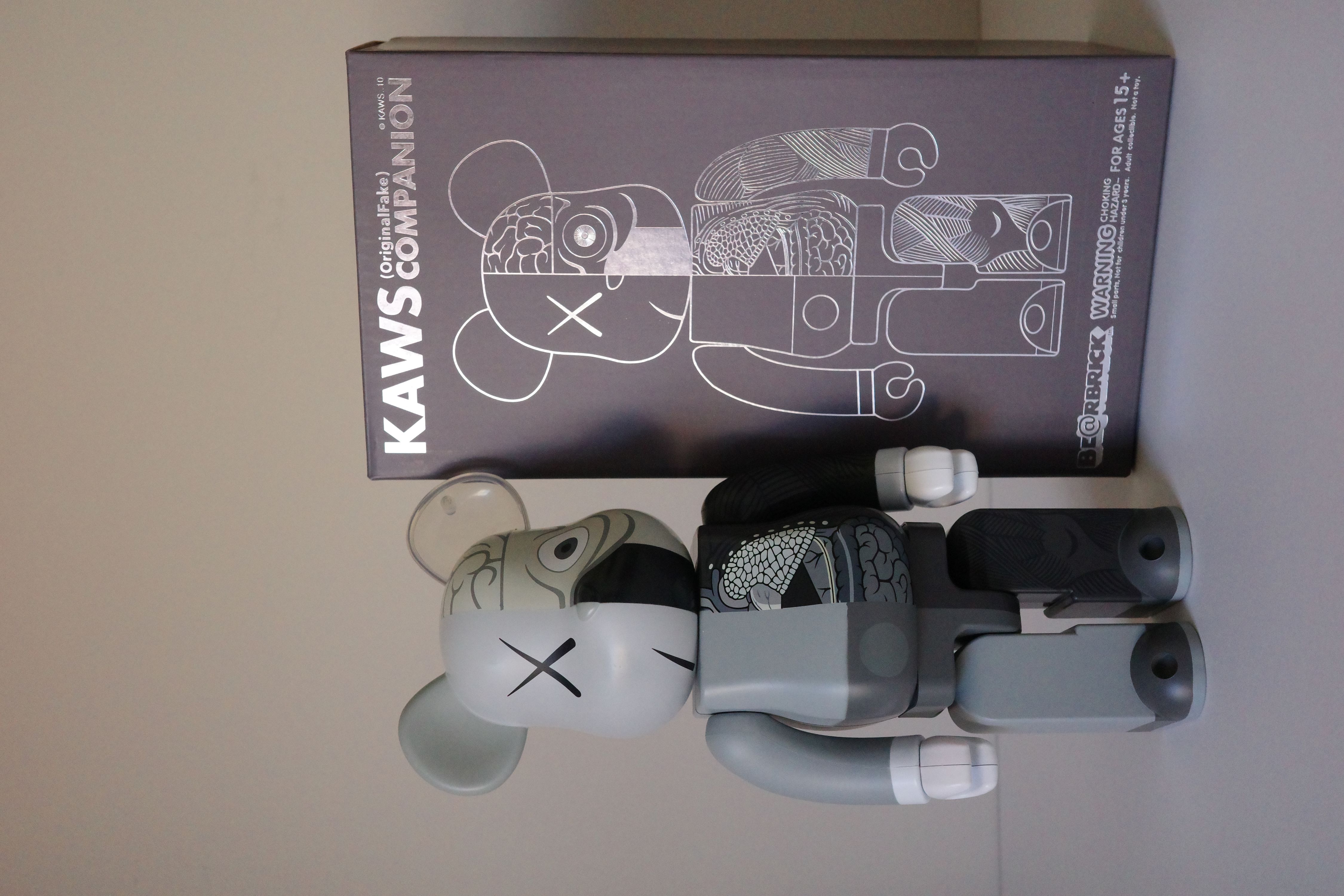 A gray and black bearbrick with a box on a white surface.