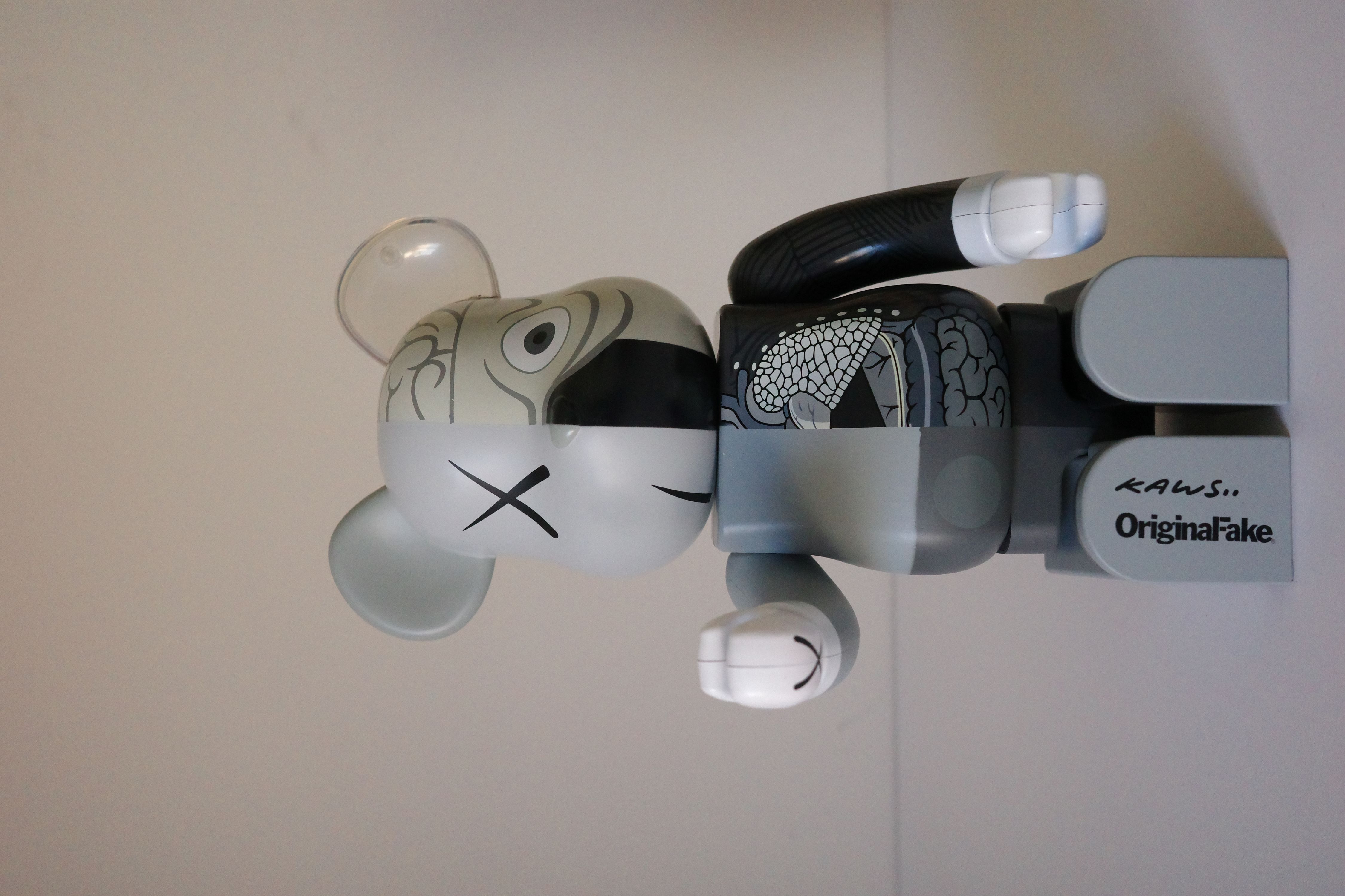 A gray and black bearbrick with a box on a white surface.