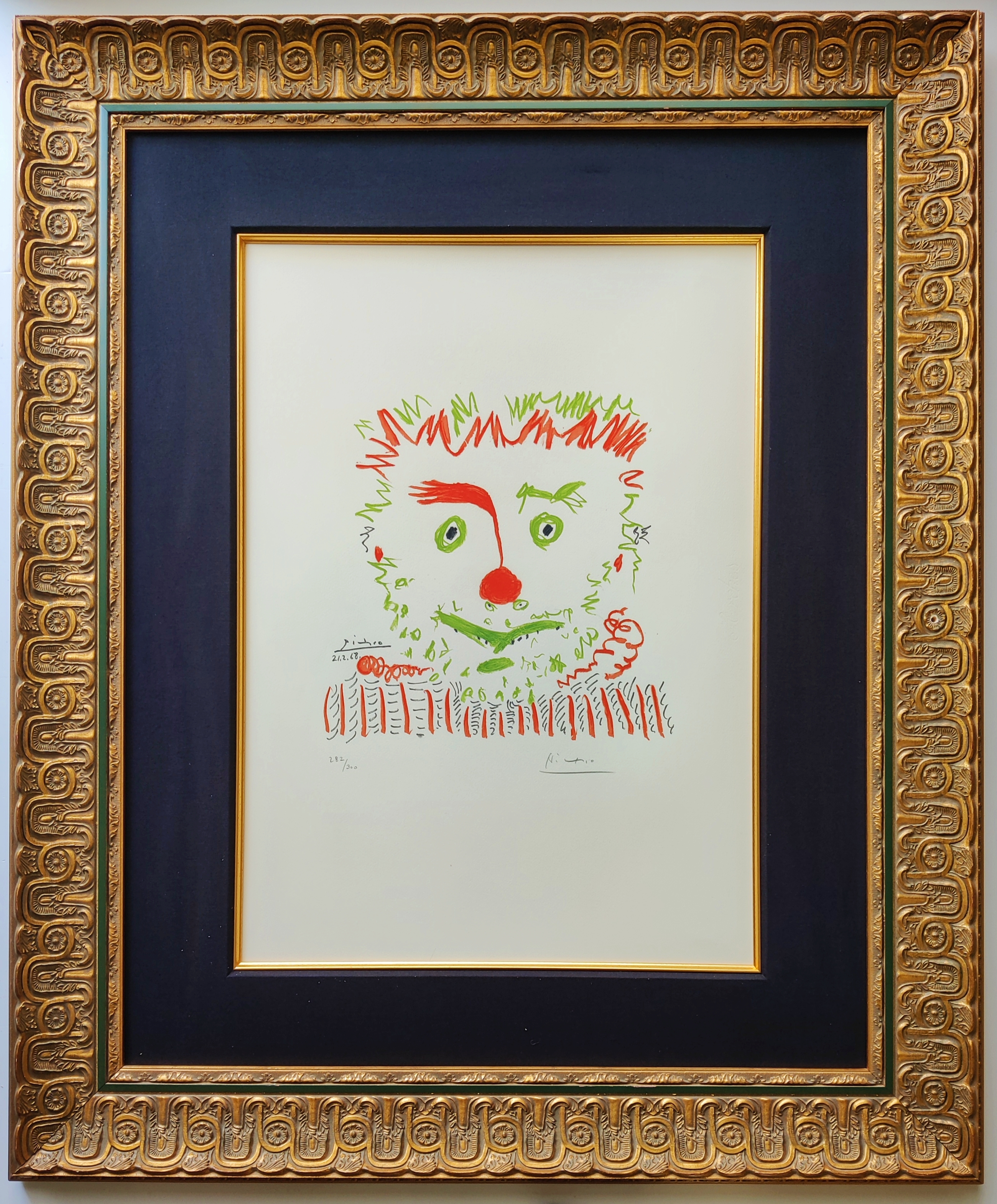 A framed picture of a clown face in a gold frame.
