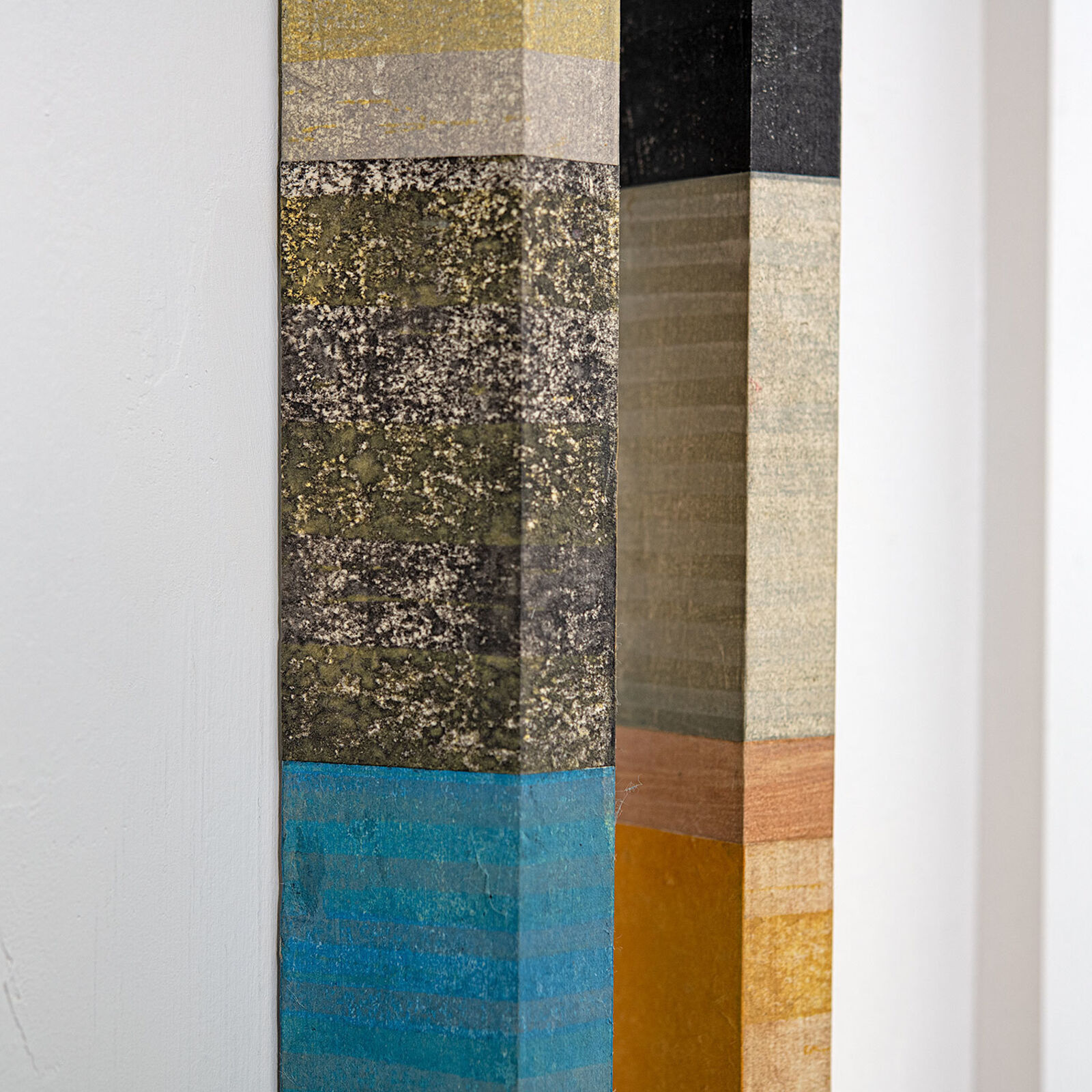 A vertical wall art piece featuring two elongated wooden slats with a patchwork of colorful, textured rectangular segments.