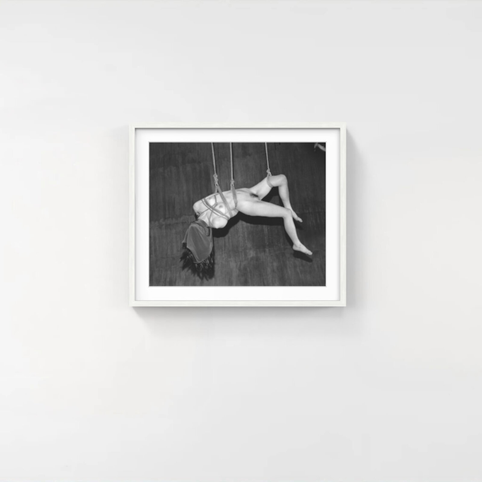 A black and white photograph of a suspended figure bound by ropes.