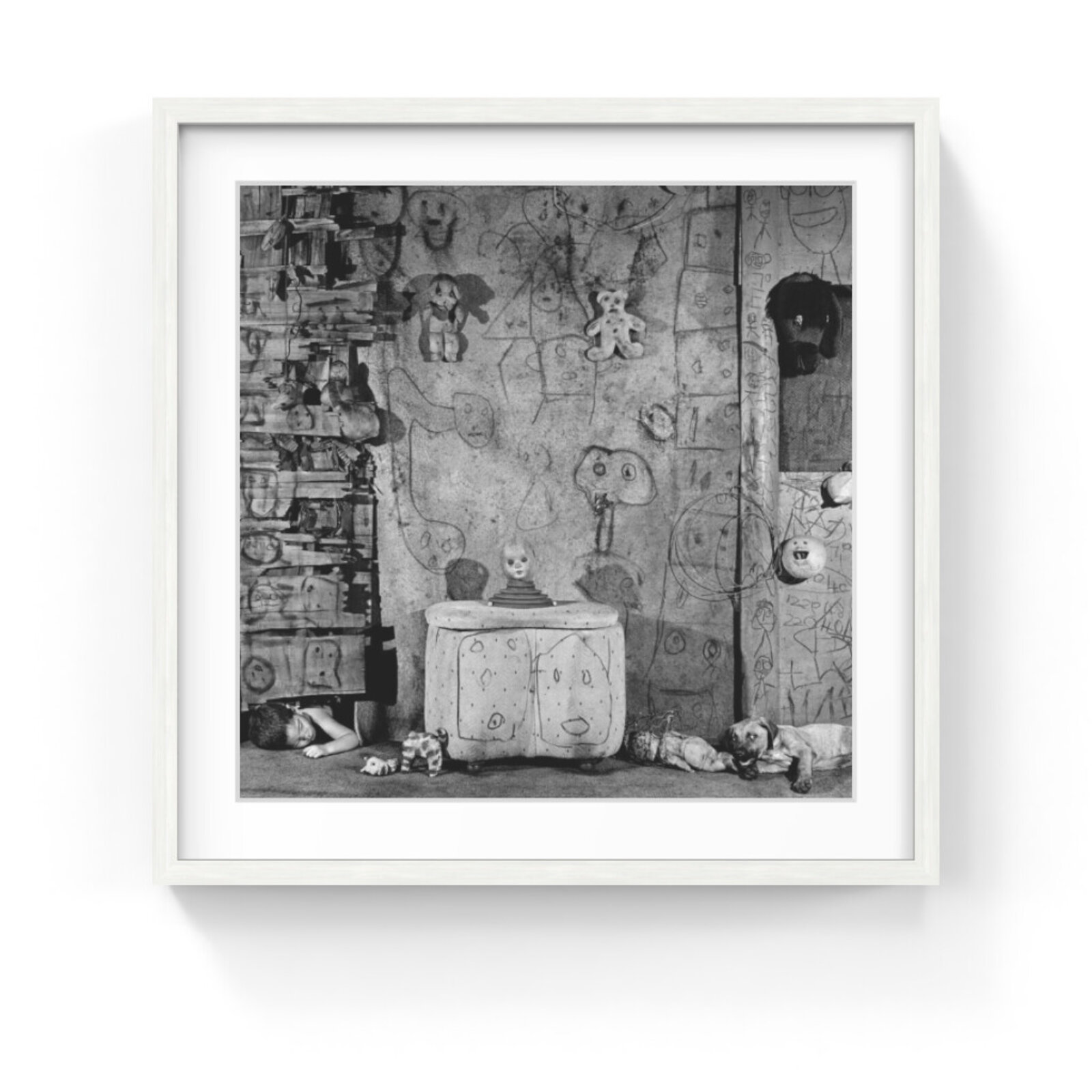 A black and white photograph of a cluttered room filled with toys, drawings, and a sleeping child.