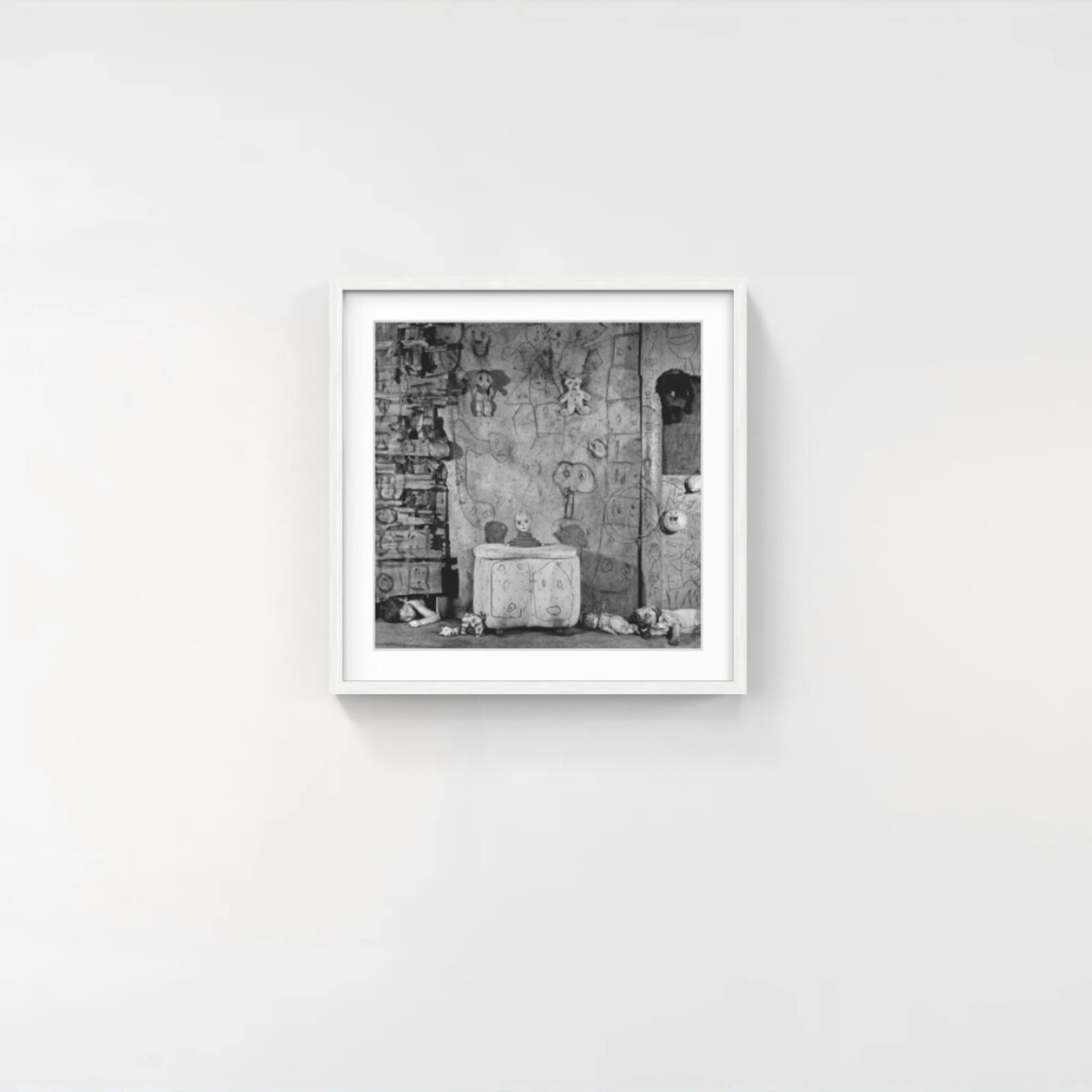 A black and white photograph of a cluttered room filled with toys, drawings, and a sleeping child.