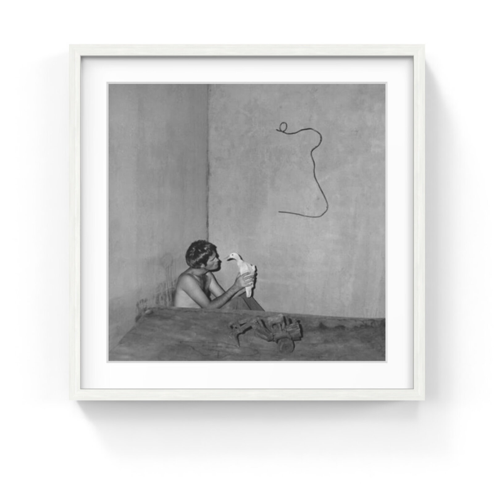 A black and white photograph of a person holding a bird in front of a wall with a squiggly line drawn on it.