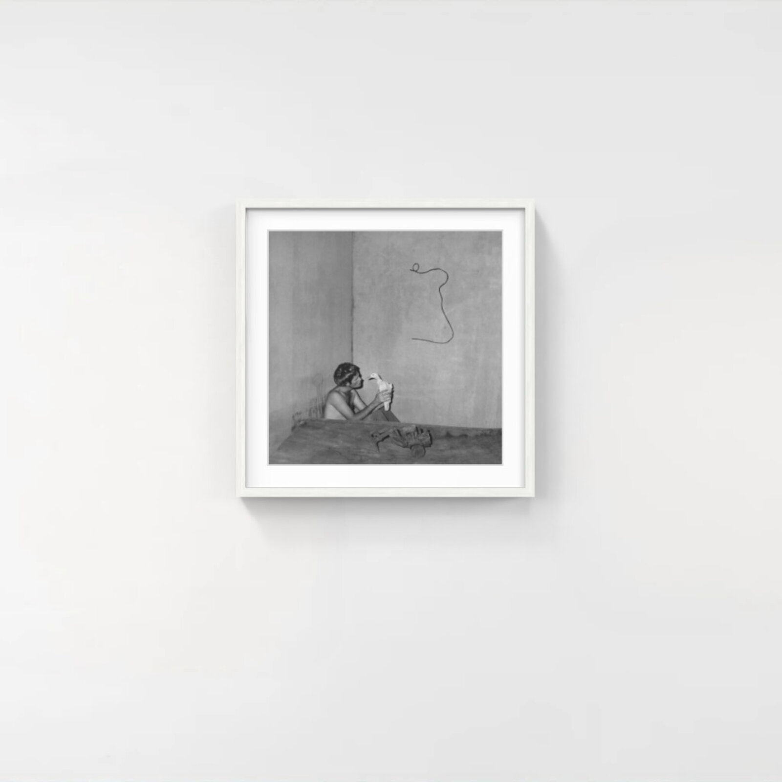 A black and white photograph of a person holding a bird in front of a wall with a squiggly line drawn on it.