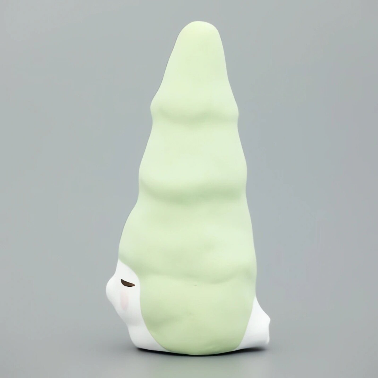 A whimsical ceramic figure with a tall, pointed green head and a serene white face.