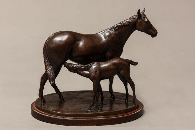 A bronze sculpture of a horse and foal on a wooden base.