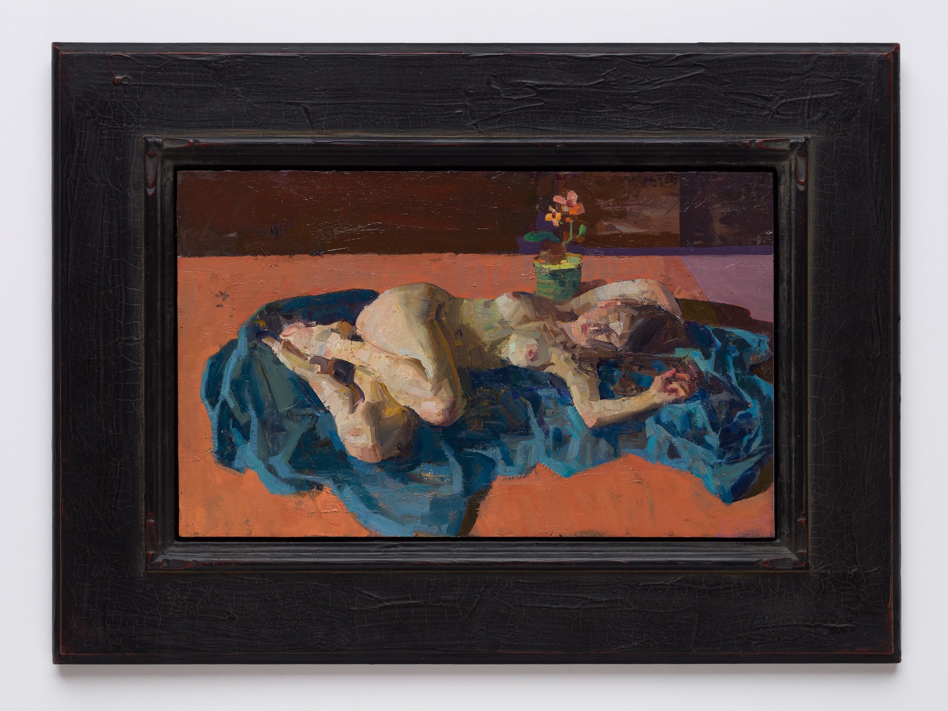 A figure rests on a blue cloth in a still life arrangement with a vase of flowers.