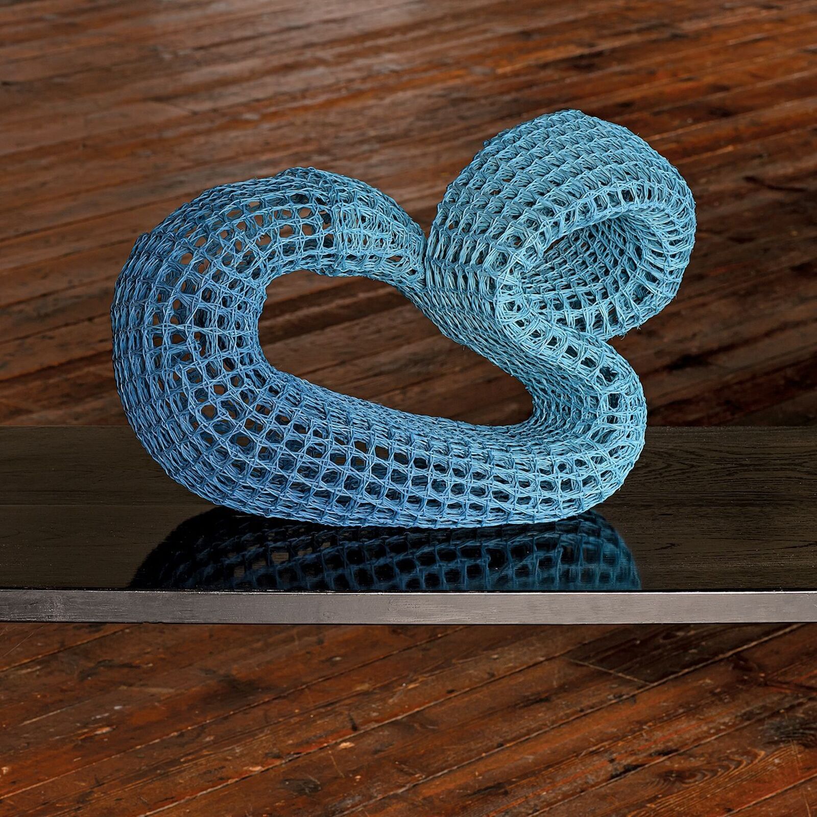 A blue mesh sculpture shaped like a figure-eight resting on a reflective surface.