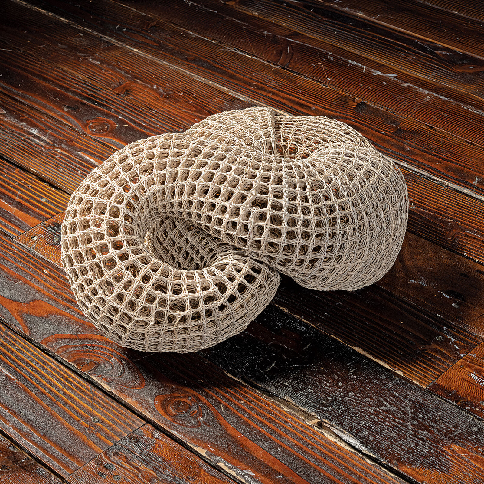 A woven, knot-shaped sculpture rests on a dark table in front of a bright window.