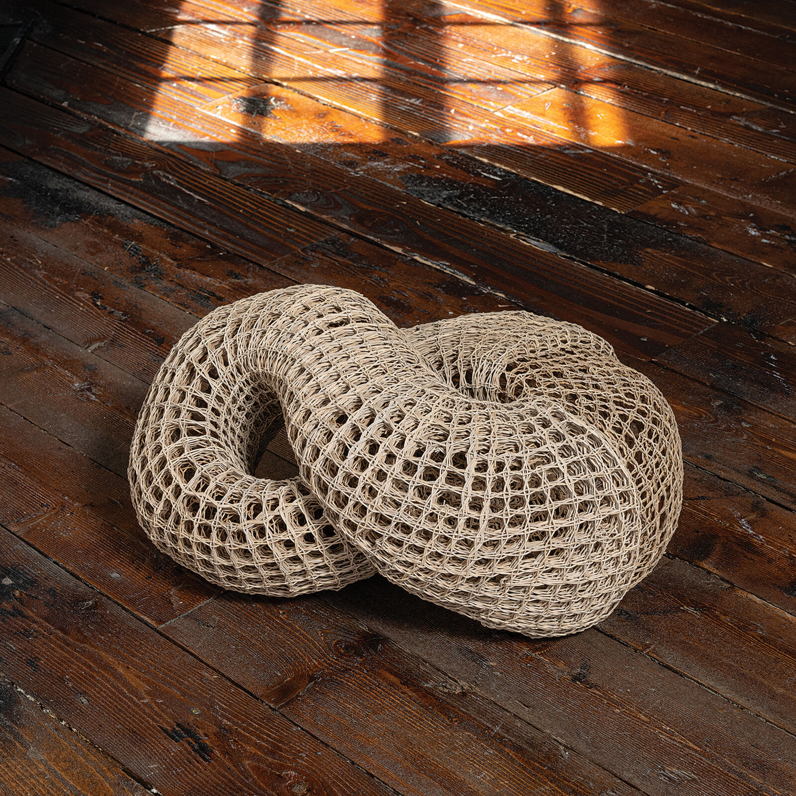 A woven, knot-shaped sculpture rests on a dark table in front of a bright window.