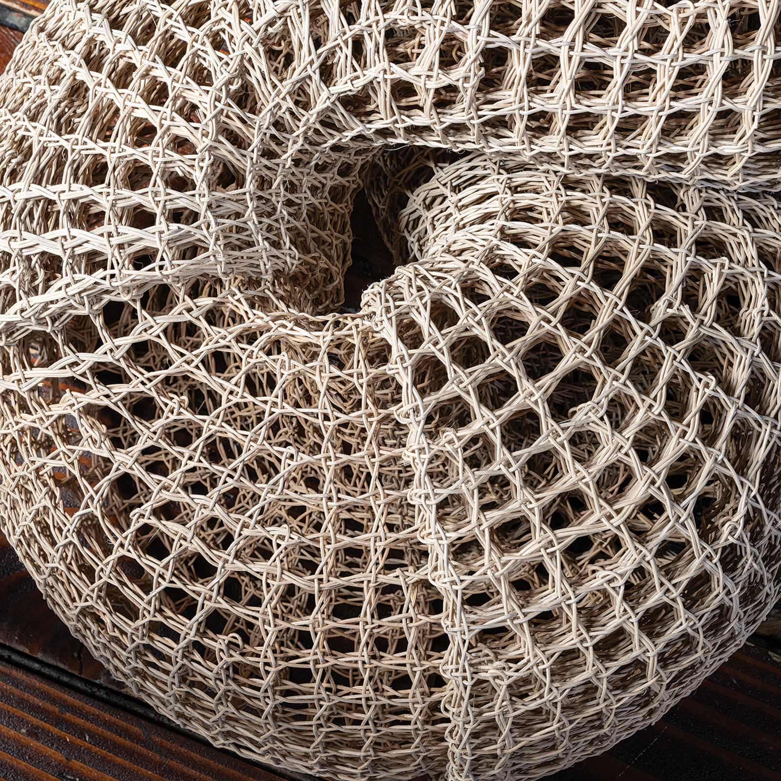 A woven, knot-shaped sculpture rests on a dark table in front of a bright window.