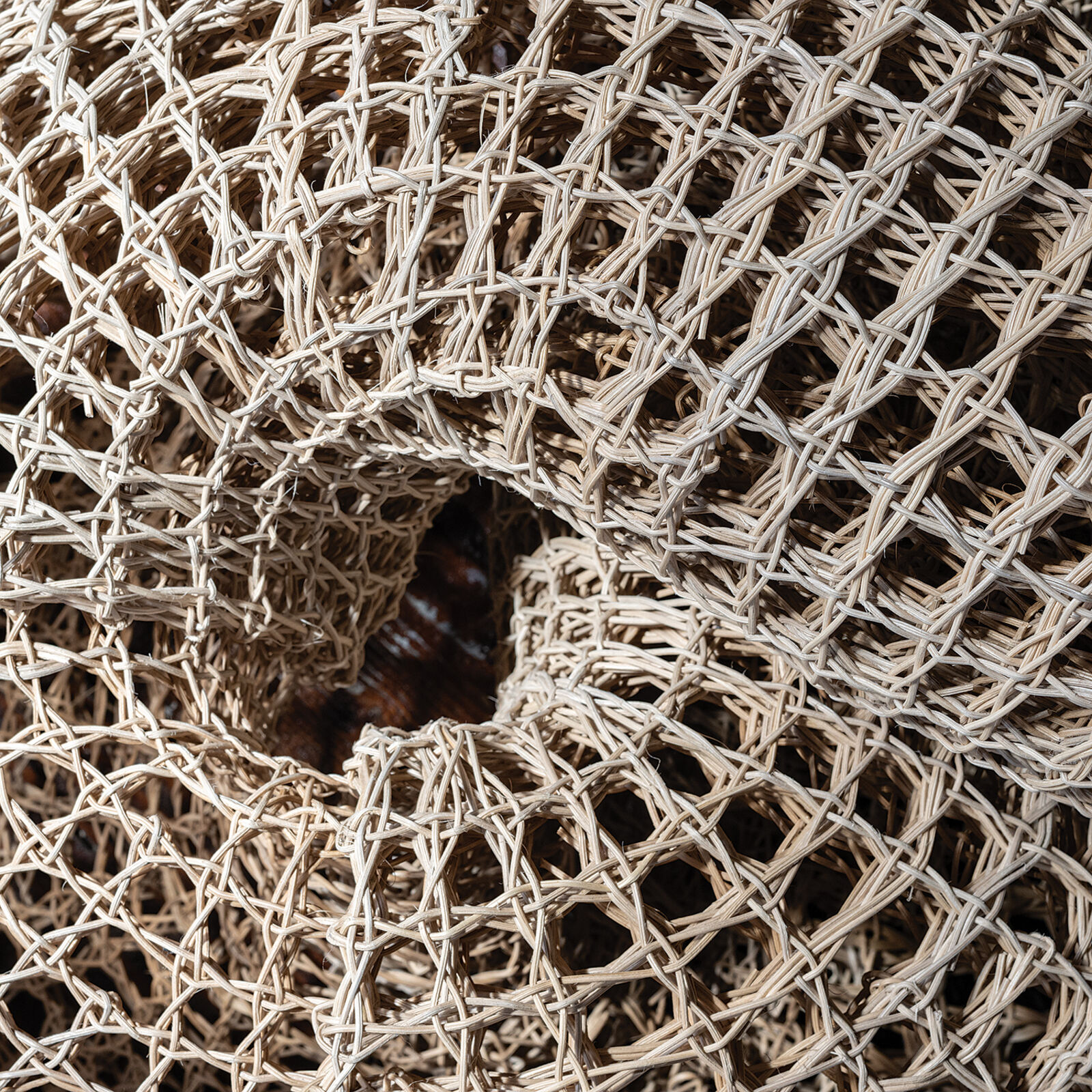 A woven, knot-shaped sculpture rests on a dark table in front of a bright window.