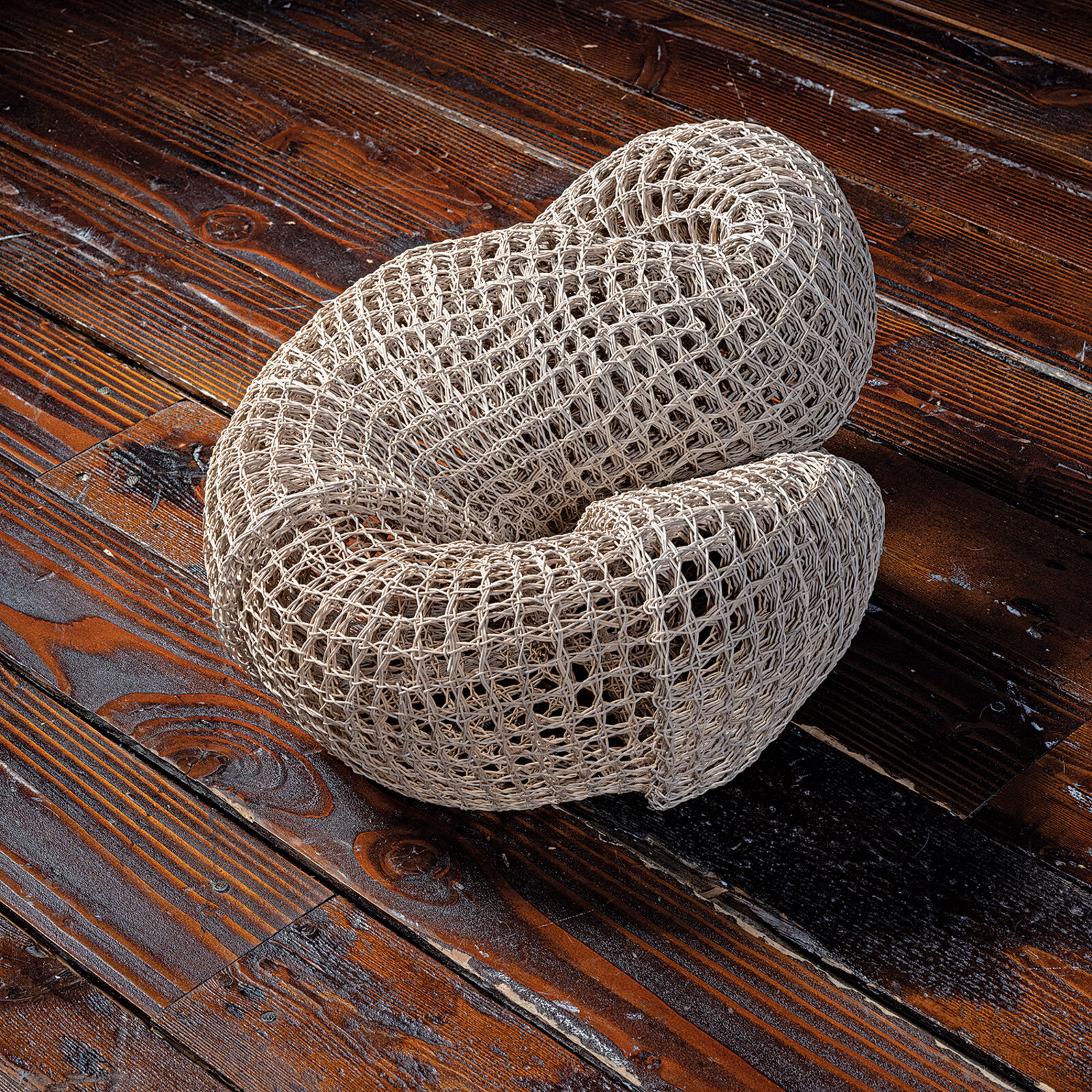 A woven, knot-shaped sculpture rests on a dark table in front of a bright window.