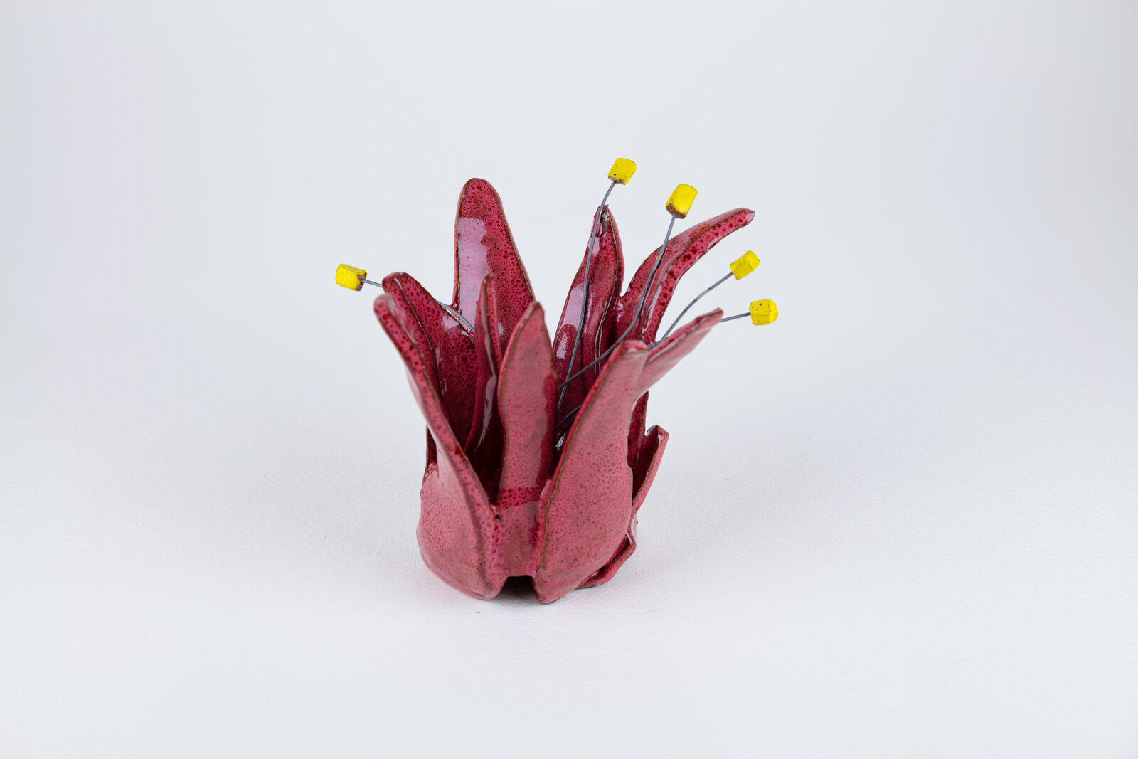 A red vase with yellow pins sticking out of it.