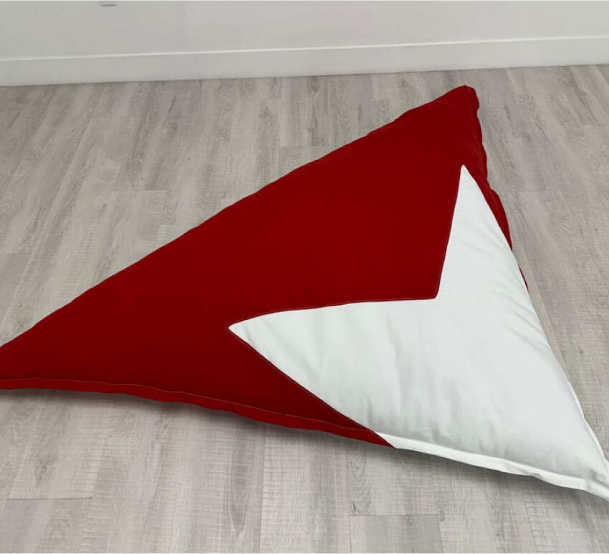 A red and white triangle shaped pillow on a wooden floor.