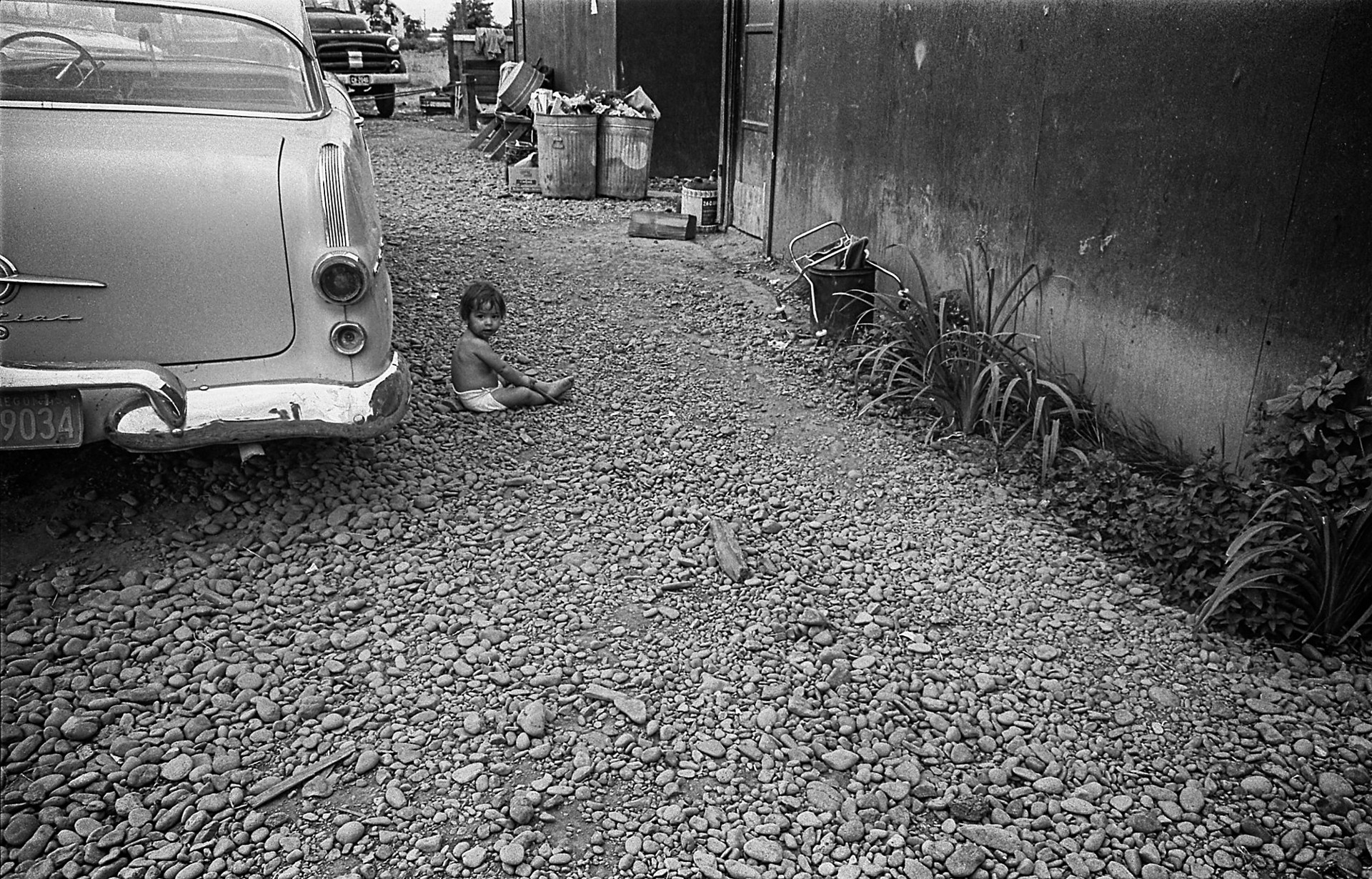A small child sitting on the ground next to a car.