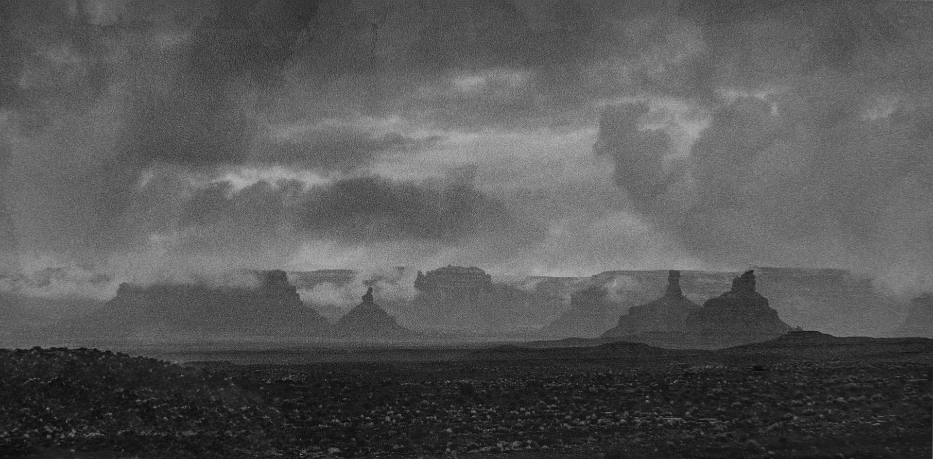 A black and white photo of a cloudy sky over a desert landscape.
