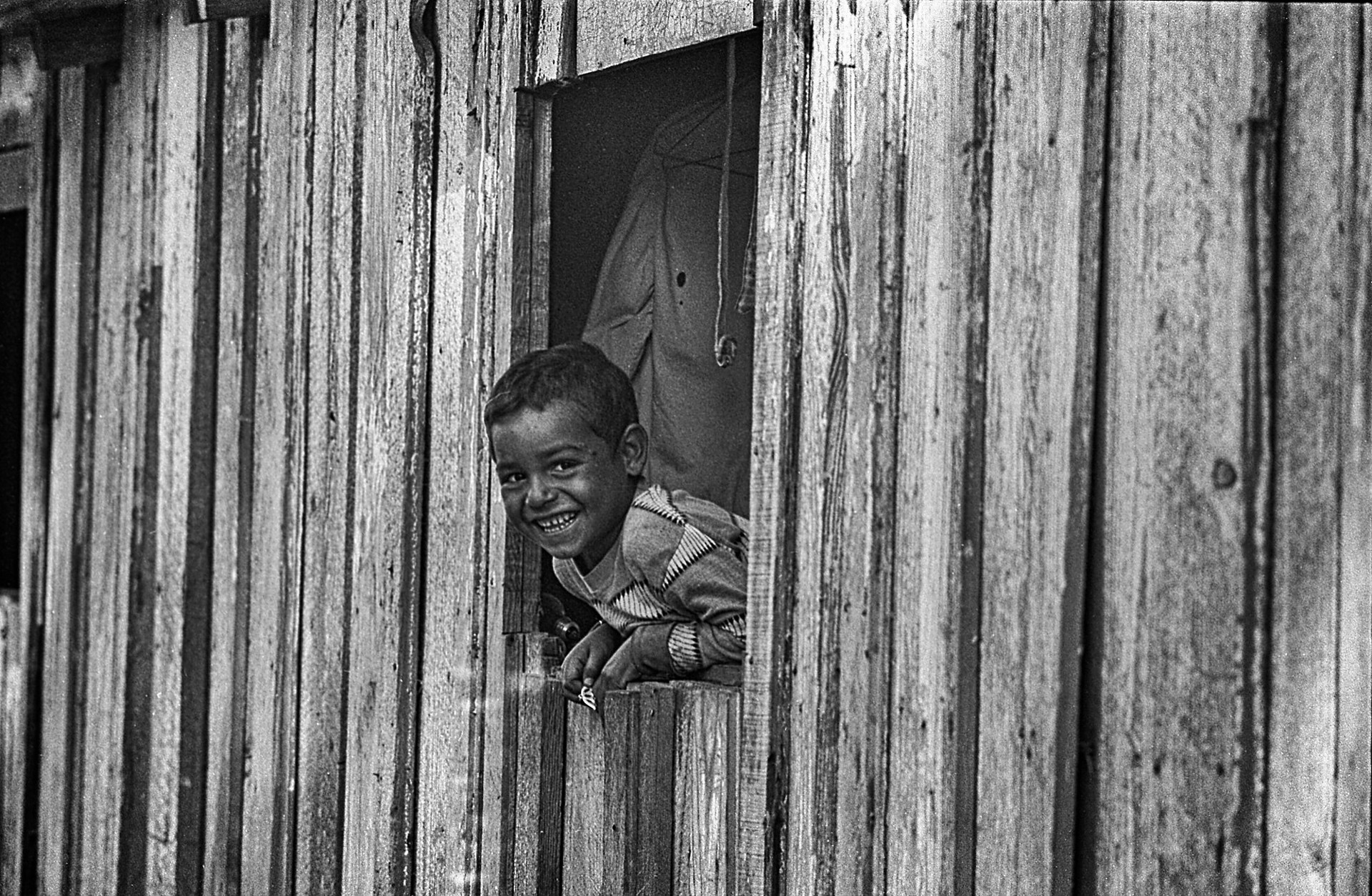 A young boy smiles as he looks out of a window.