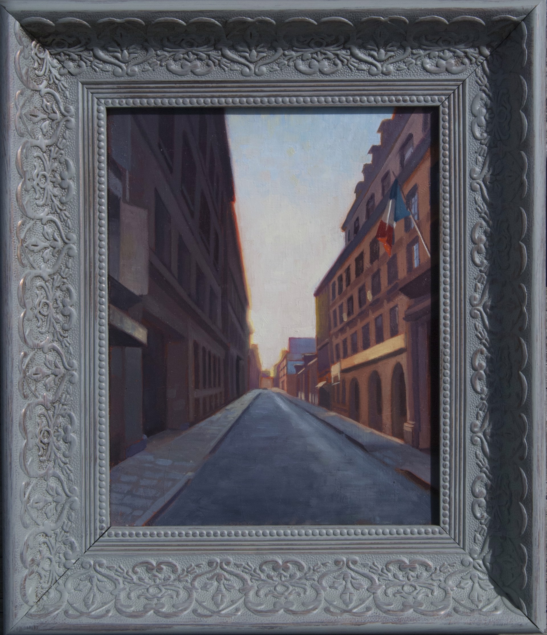 A framed painting of a quiet European street at dusk with a small Italian flag.