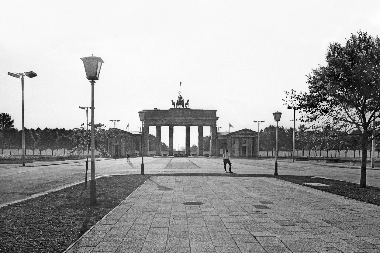 A black and white photo of a man walking in front of a gate.