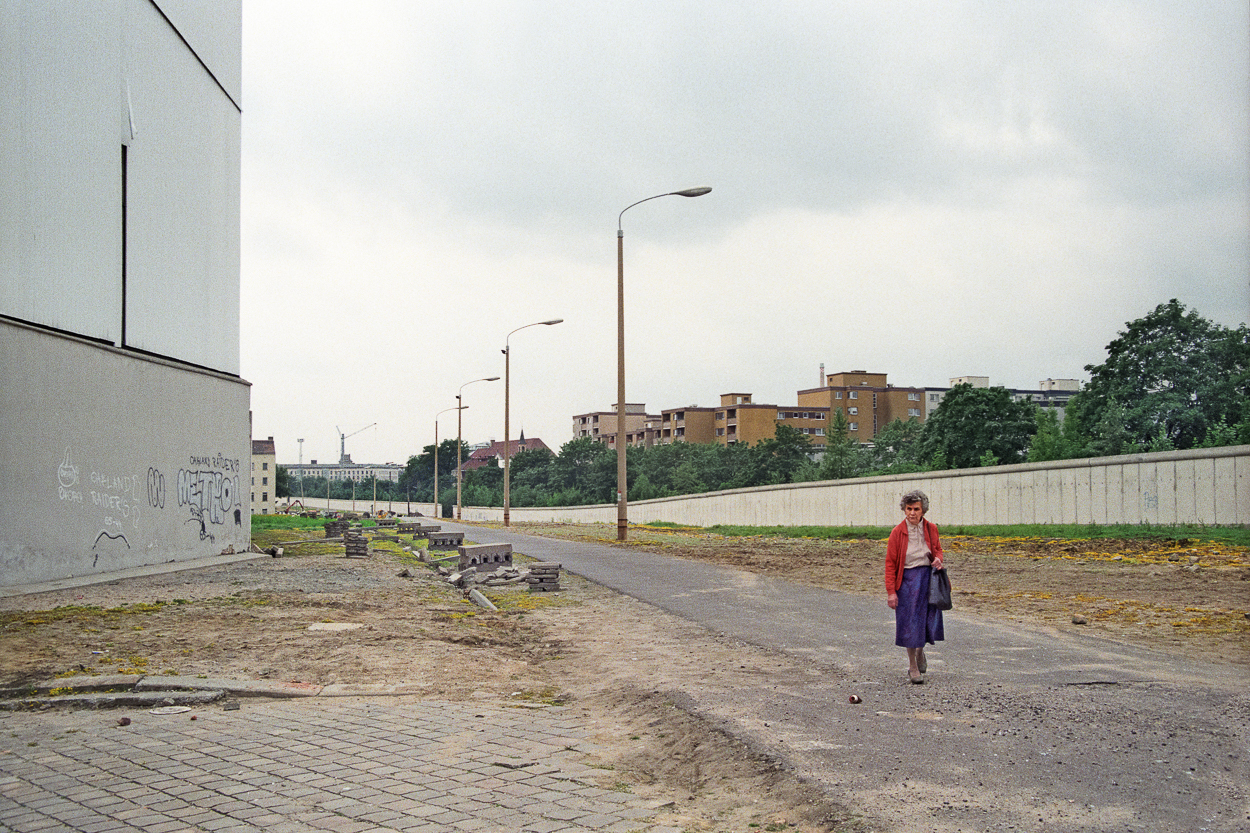 A woman walking down a dirt road next to a wall.