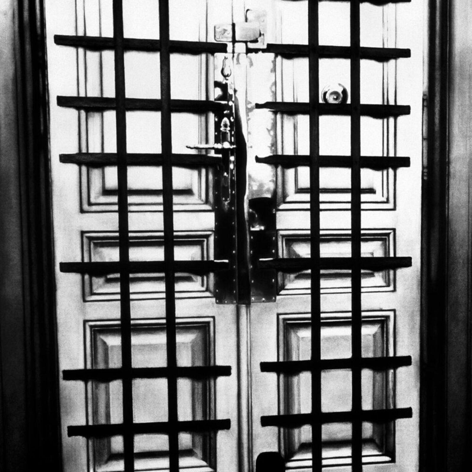 A black and white photo of a door with bars on it.