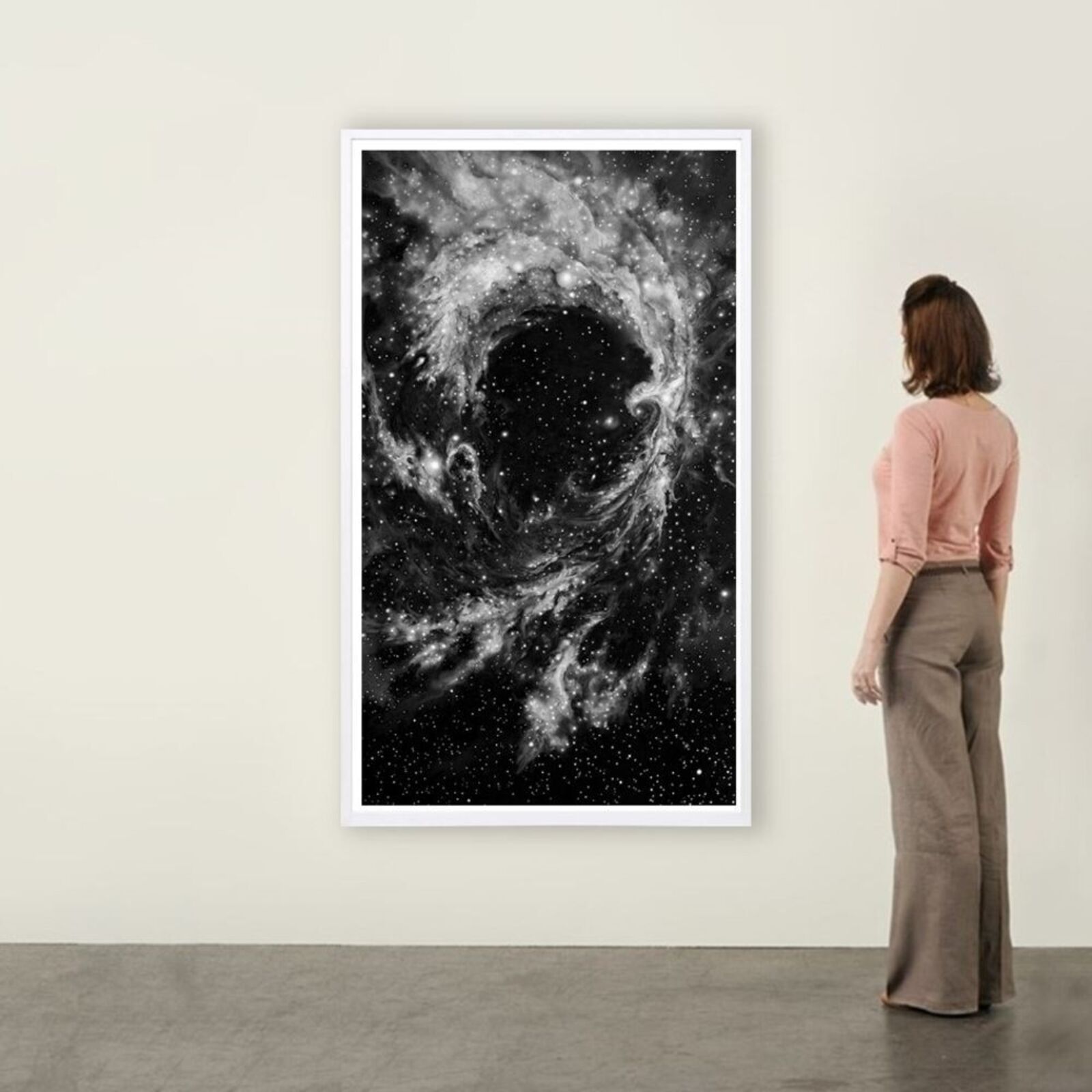 A framed black-and-white print of a swirling cosmic nebula against a minimalist interior wall.